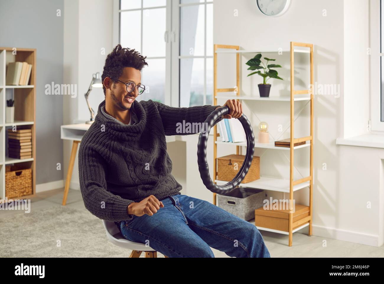 Funny, happy man sitting on a chair at home and pretending to drive an invisible car Stock Photo