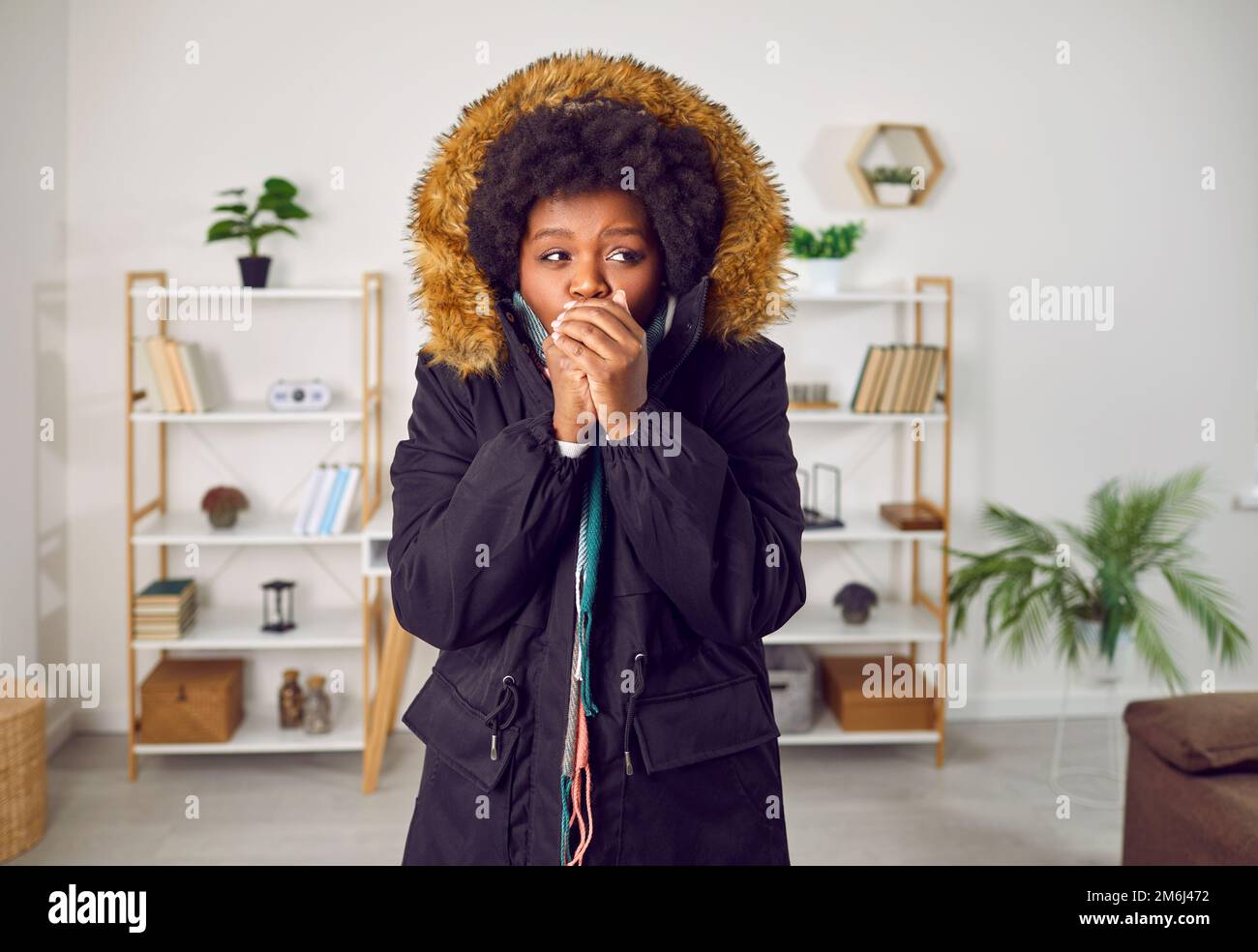 African American woman freezing and wearing warm clothes indoors during a cold winter Stock Photo