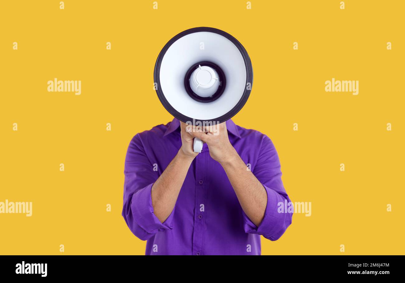 Man hiding his face behind loudspeaker makes loud announcement or advertisement on orange background Stock Photo