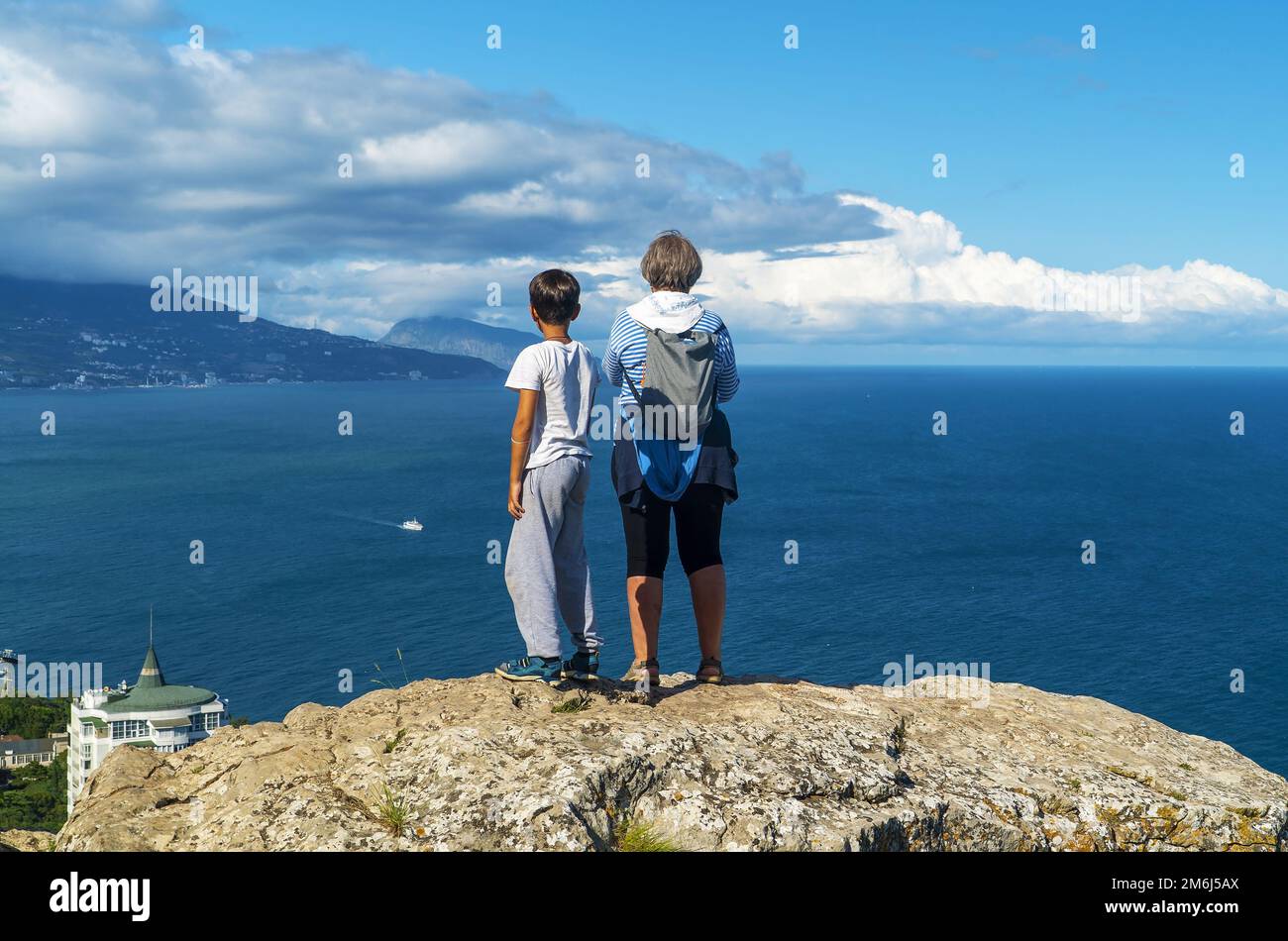 Grandmother and grandson are standing on the edge of a cliff high above the sea. Stock Photo