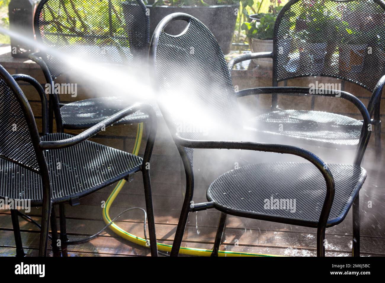 Power surface washing. Man cleaning terrace with a power washer. High water pressure cleaner on wooden terrace surface and outdoor furniture. Stock Photo