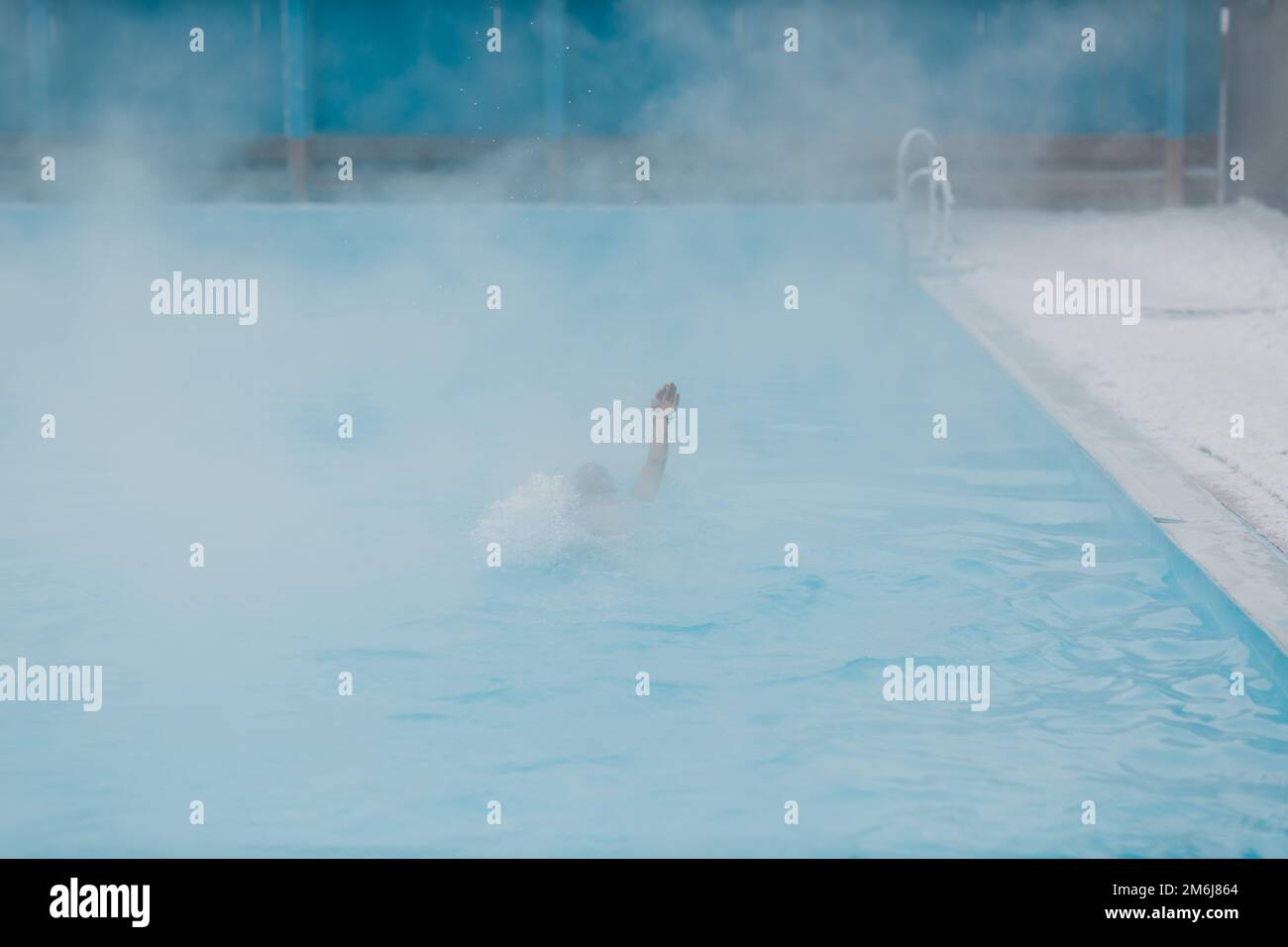 Fit swimmer male training swim in open winter swimming pool with fog. Geothermal outdoor spa concept. Stock Photo