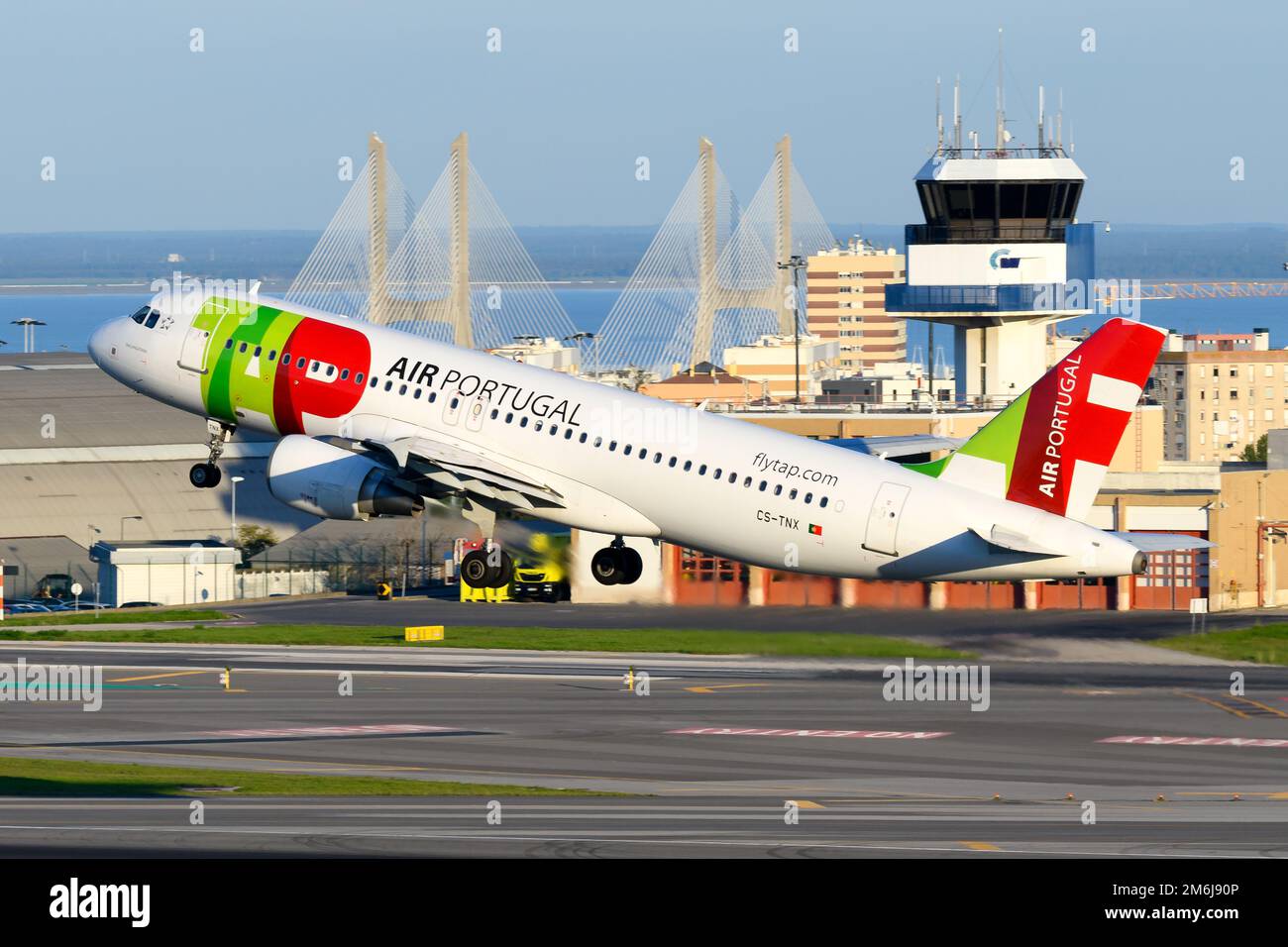 TAP Air Portugal Airbus A320 aircraft taking off from Lisbon Airport with Vasco da Gama Bridge behind. Airplane of TAP and Lisbon ATC tower. Stock Photo