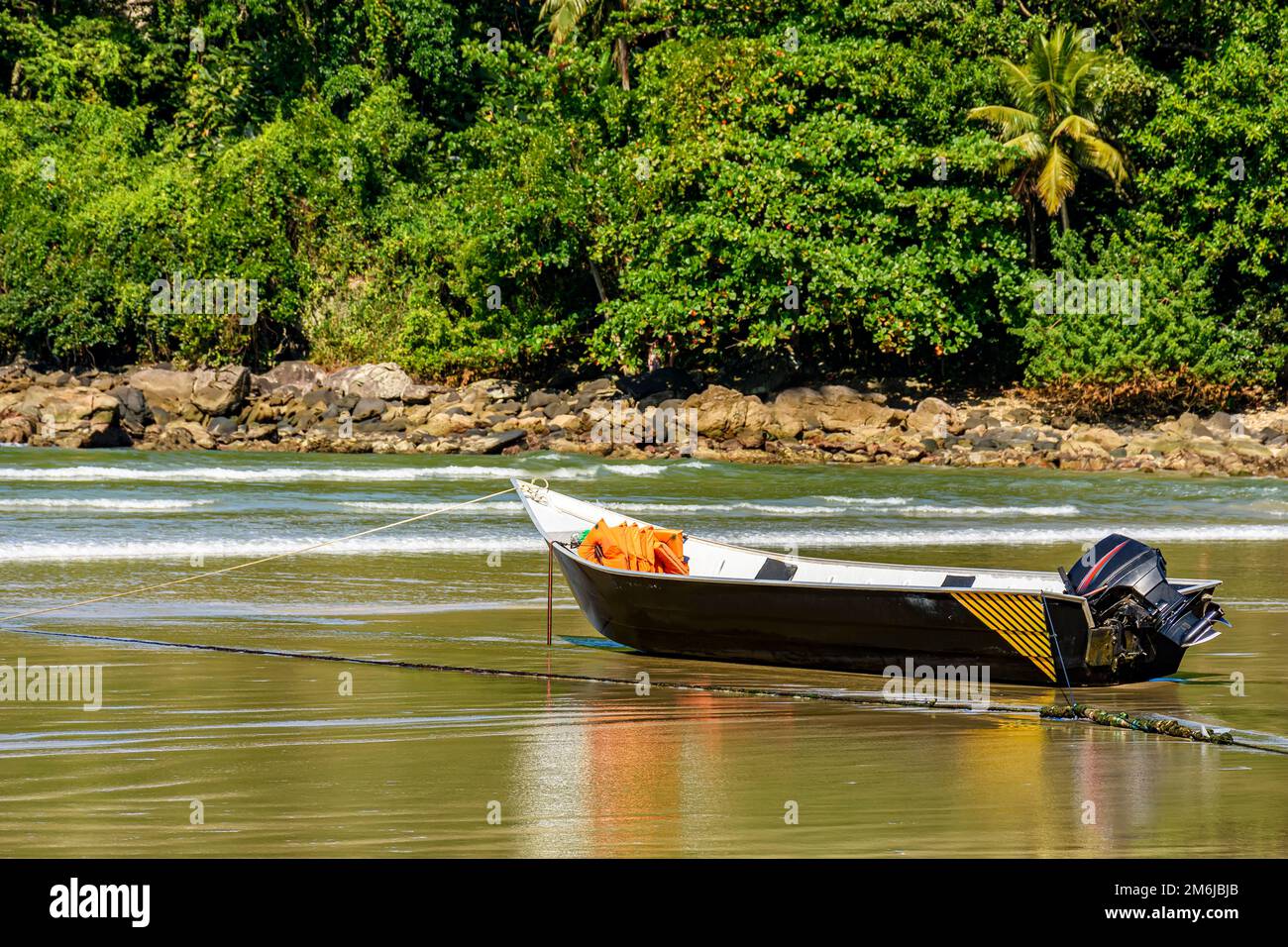 Speedboat standing on the sand of the beach with the rocks and rainforest in the background Stock Photo