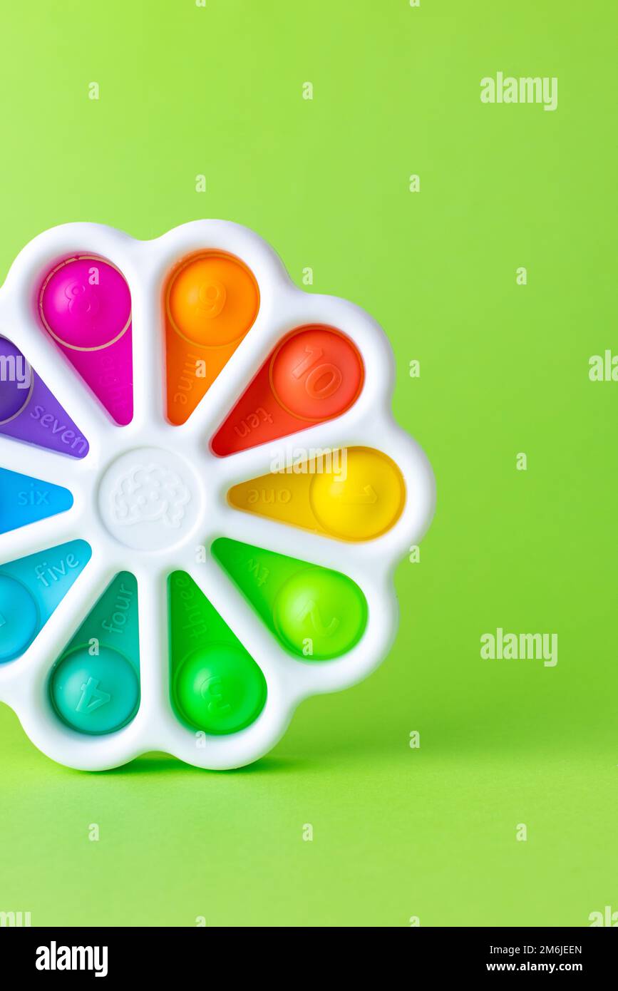 Presses with a finger anti-stress toy pop it on green background. Colorful silicone poppit toy, bubble fidget, simple-dimple Stock Photo