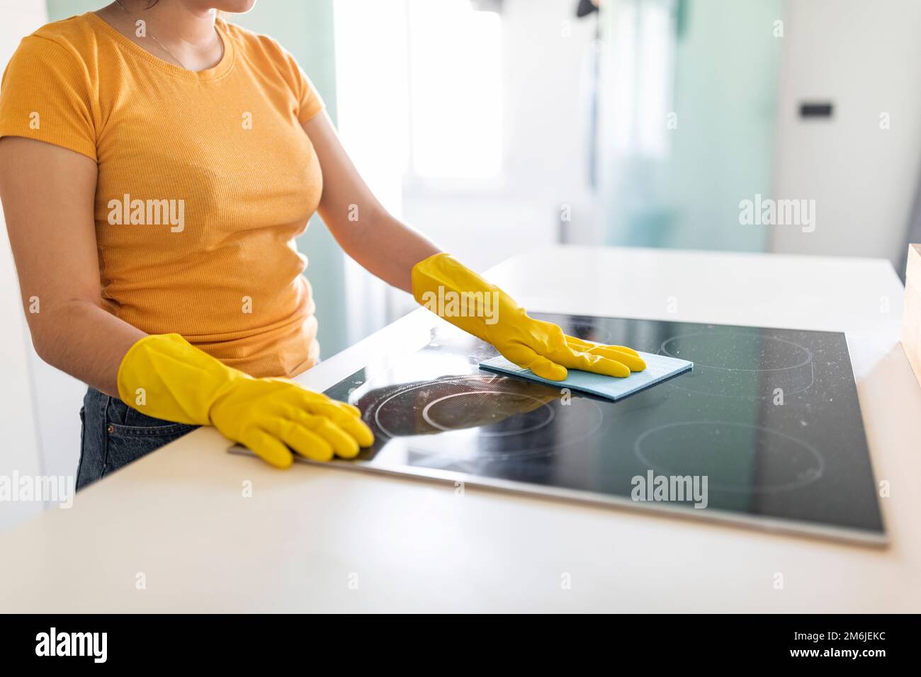 Housekeeping Concept. Young Woman In Rubber Gloves Cleaning Induction