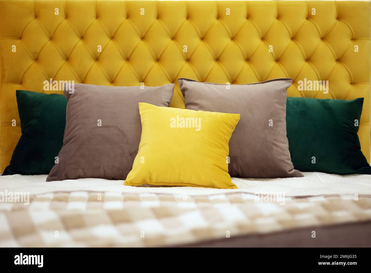 Square pillows of various colors and sizes lie on the bed with a soft yellow velvet headboard with capitones. Selective focus. Stock Photo