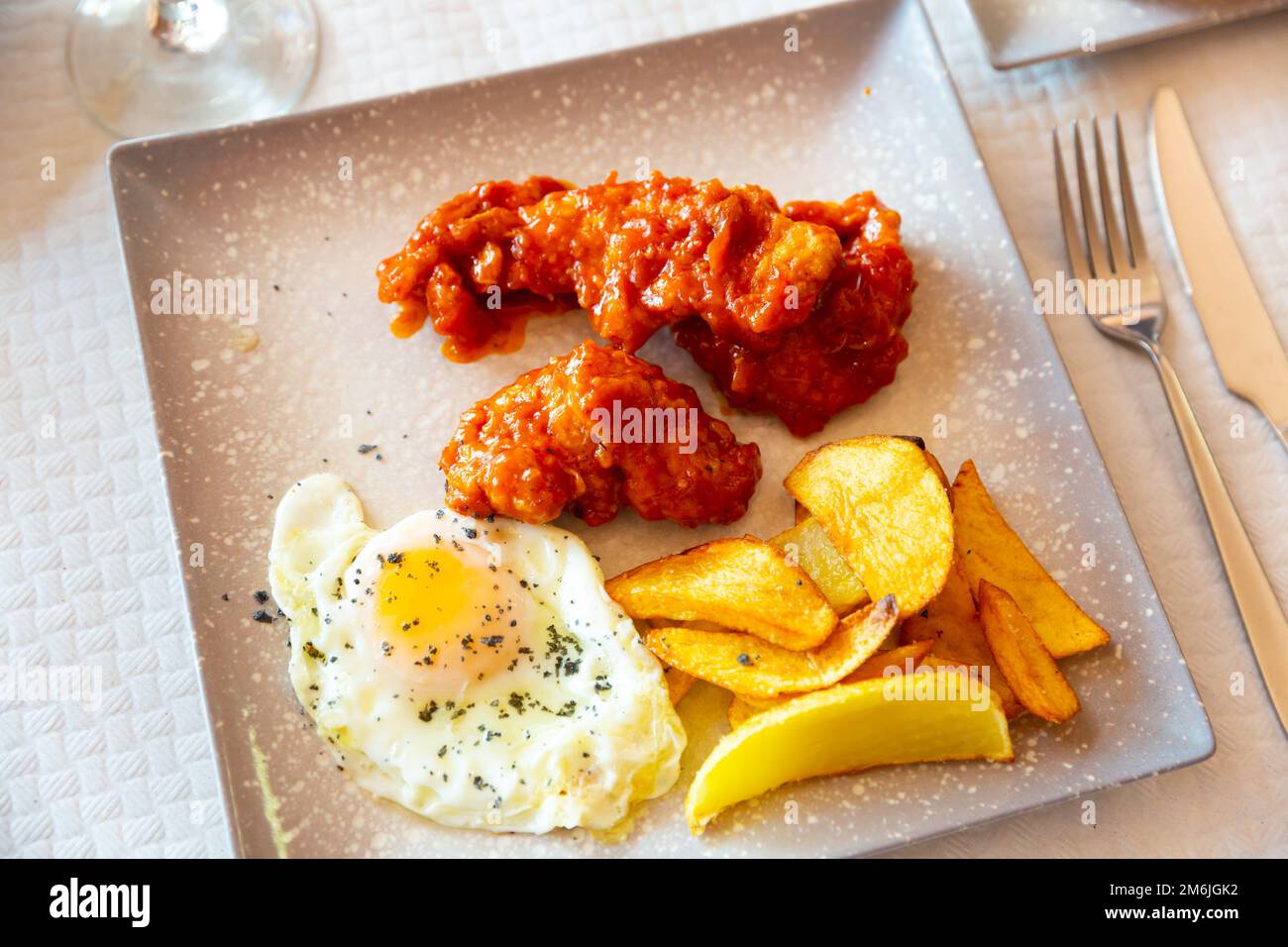 Baked potatoes with chicken in sauce and fried egg at plate Stock Photo