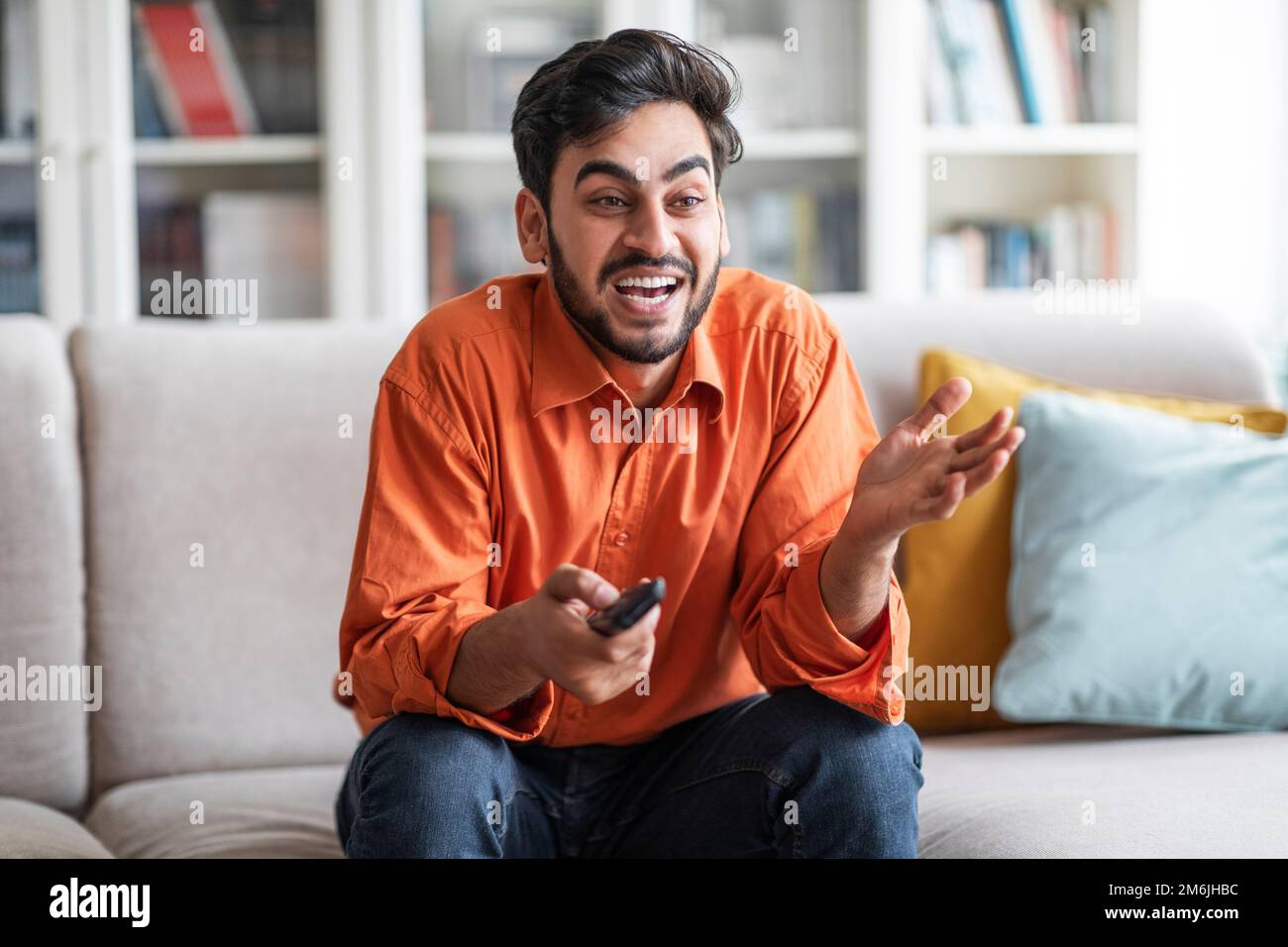 Happy arabic man watching TV at home, laughing Stock Photo