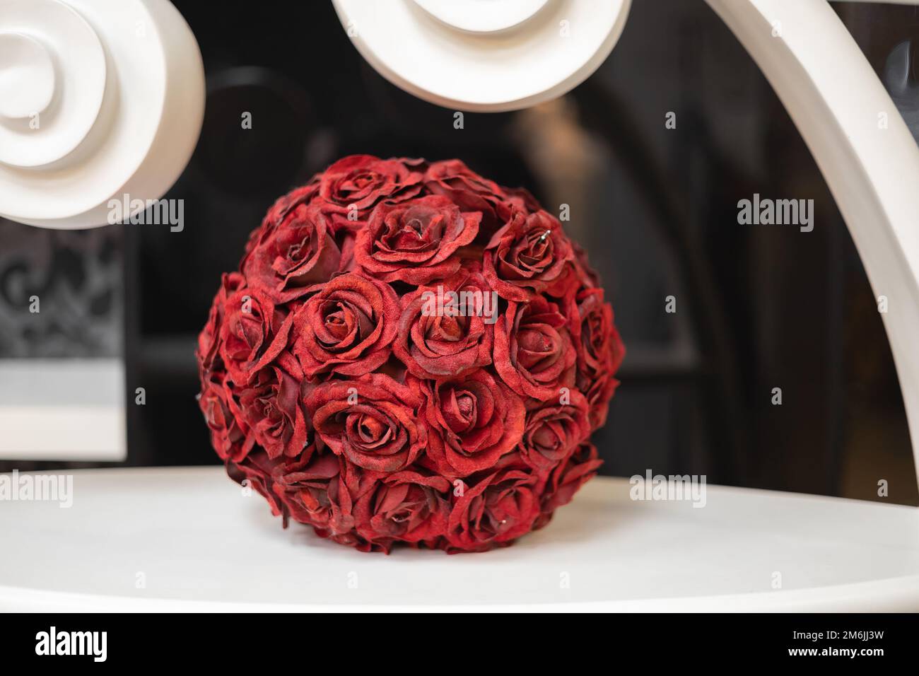 A decorative ball made from red rose sepals stands on a white surface indoors. Interior decoration. Stock Photo