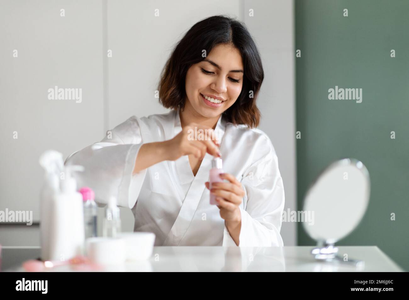 Smiling pretty young woman using face serum at home Stock Photo