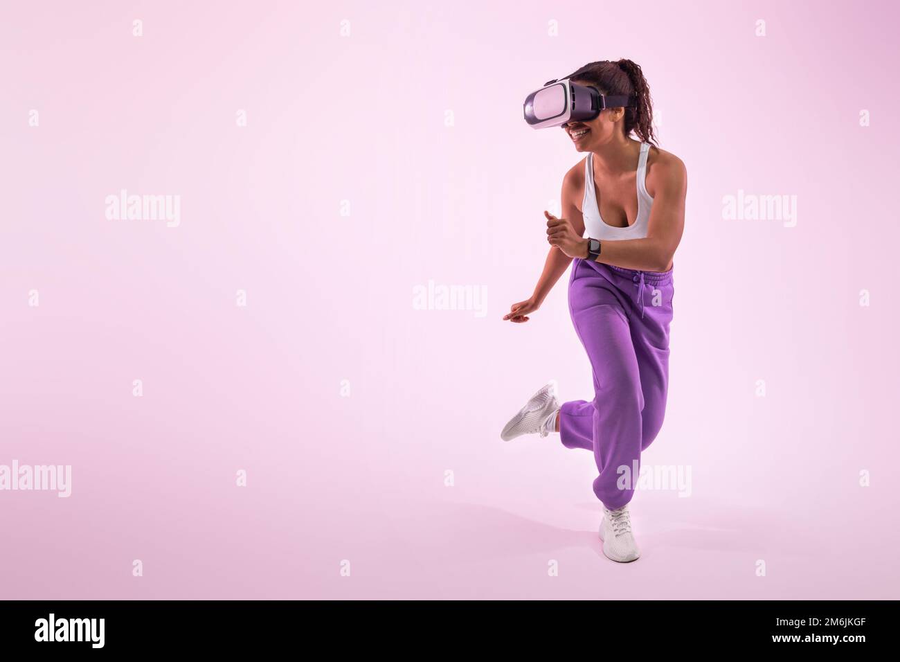 Experiencing the metaverse. African american lady gaming with virtual reality goggles, pink background, free space Stock Photo