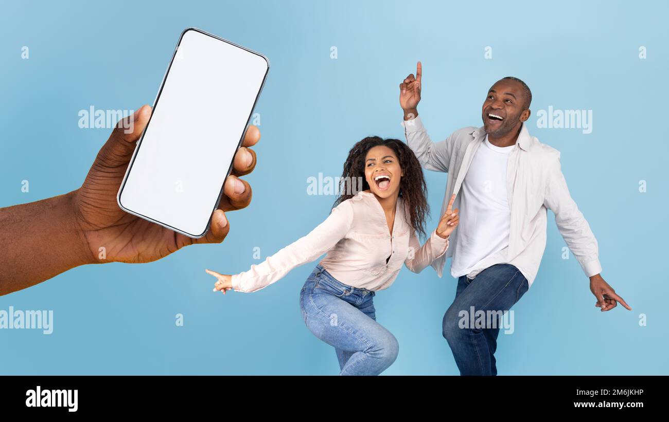 Great offer. Happy black couple dancing and looking at giant cell phone showing blank space for mock up Stock Photo
