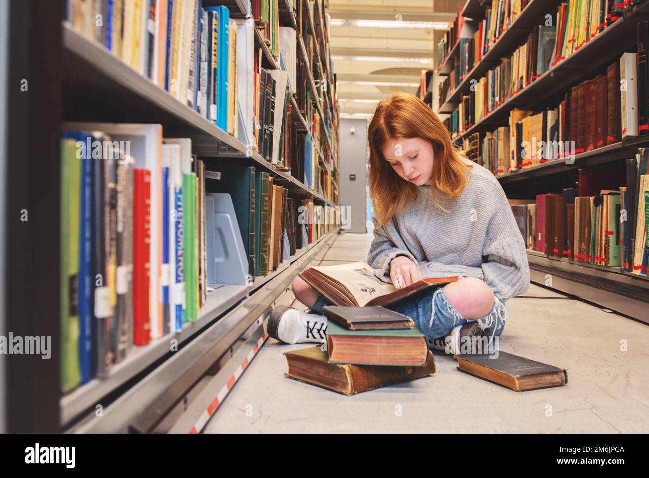 Teen Redhead Girl Sitting With Pile of Books in Library Stock Photo - Alamy
