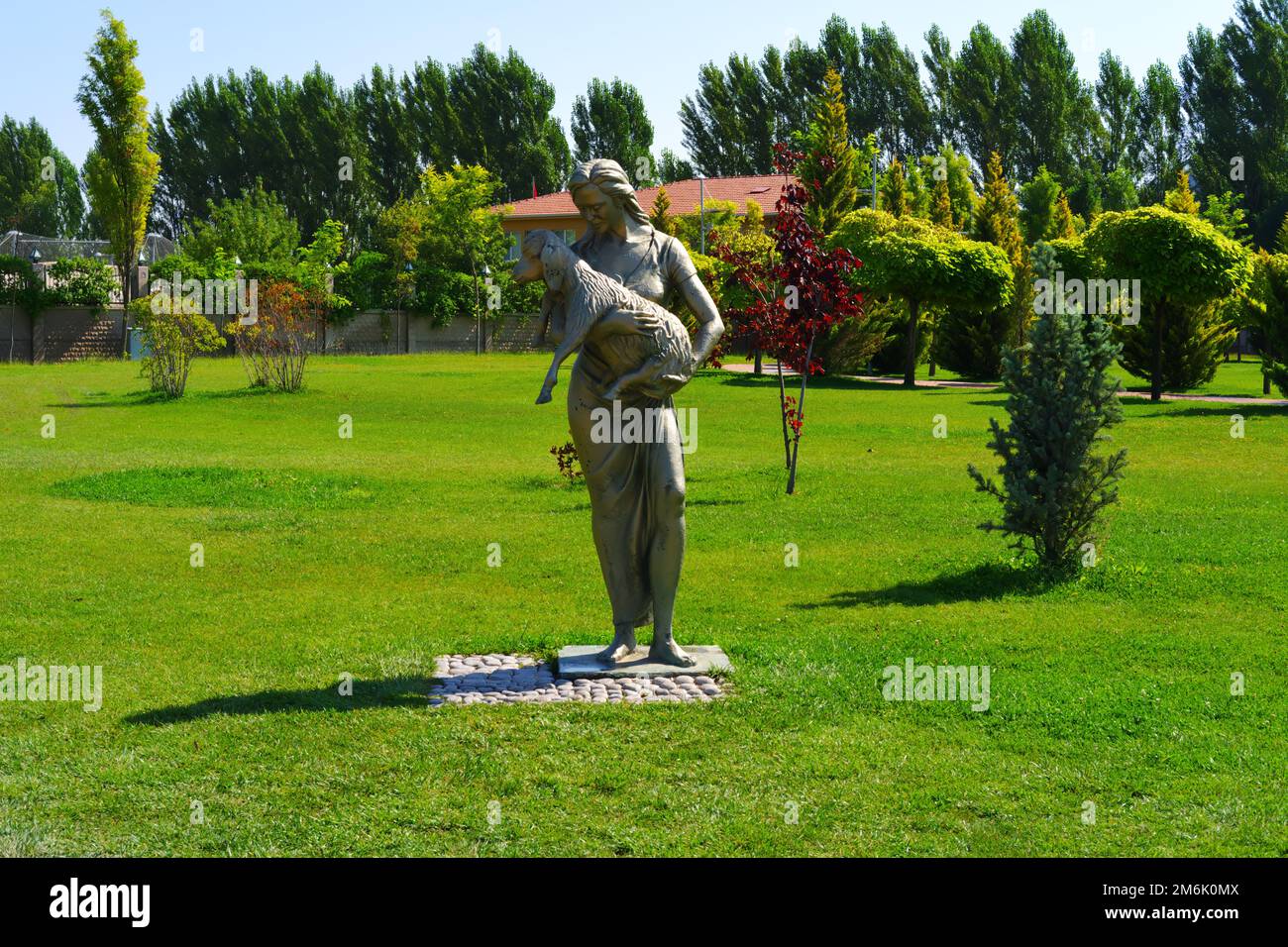 Statue of woman holding lamb on hands at park within trees in a sunny day Stock Photo