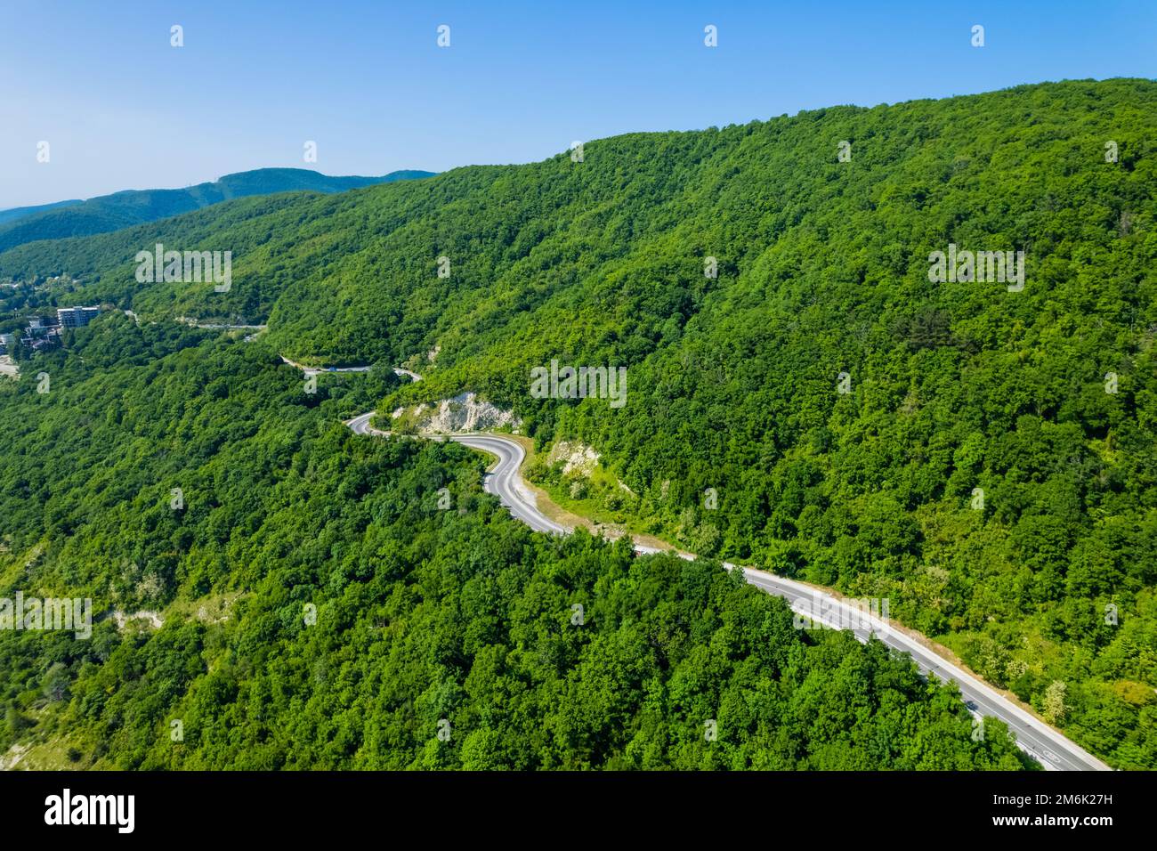 Winding road is meandering between blue sea and green mountains. Aerial view of car driving along the winding mountain road in S Stock Photo