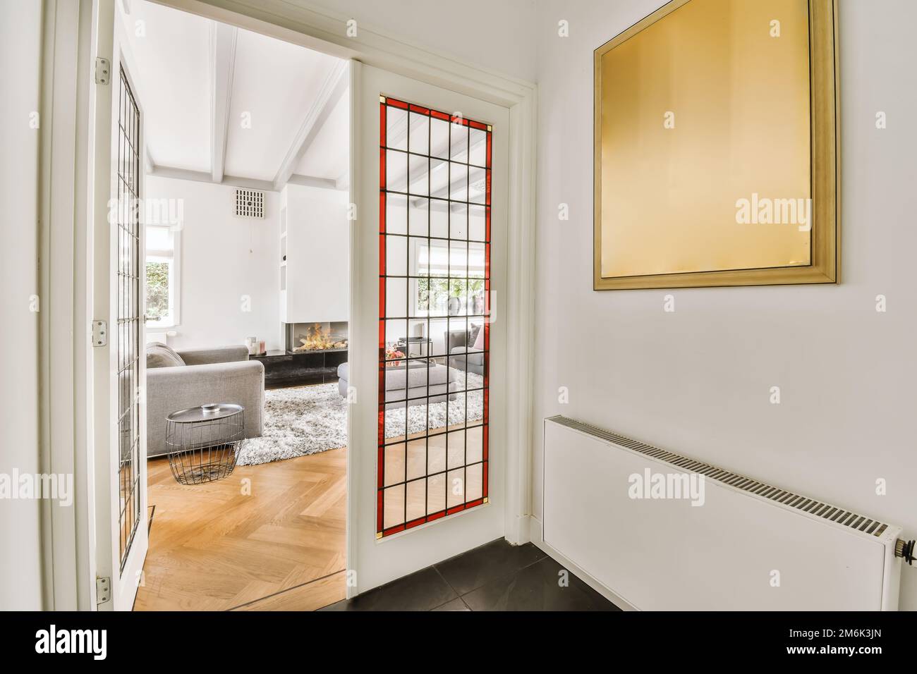 a living room with white walls and wood flooring, framed by a red glass paneled door that leads to the entryway Stock Photo