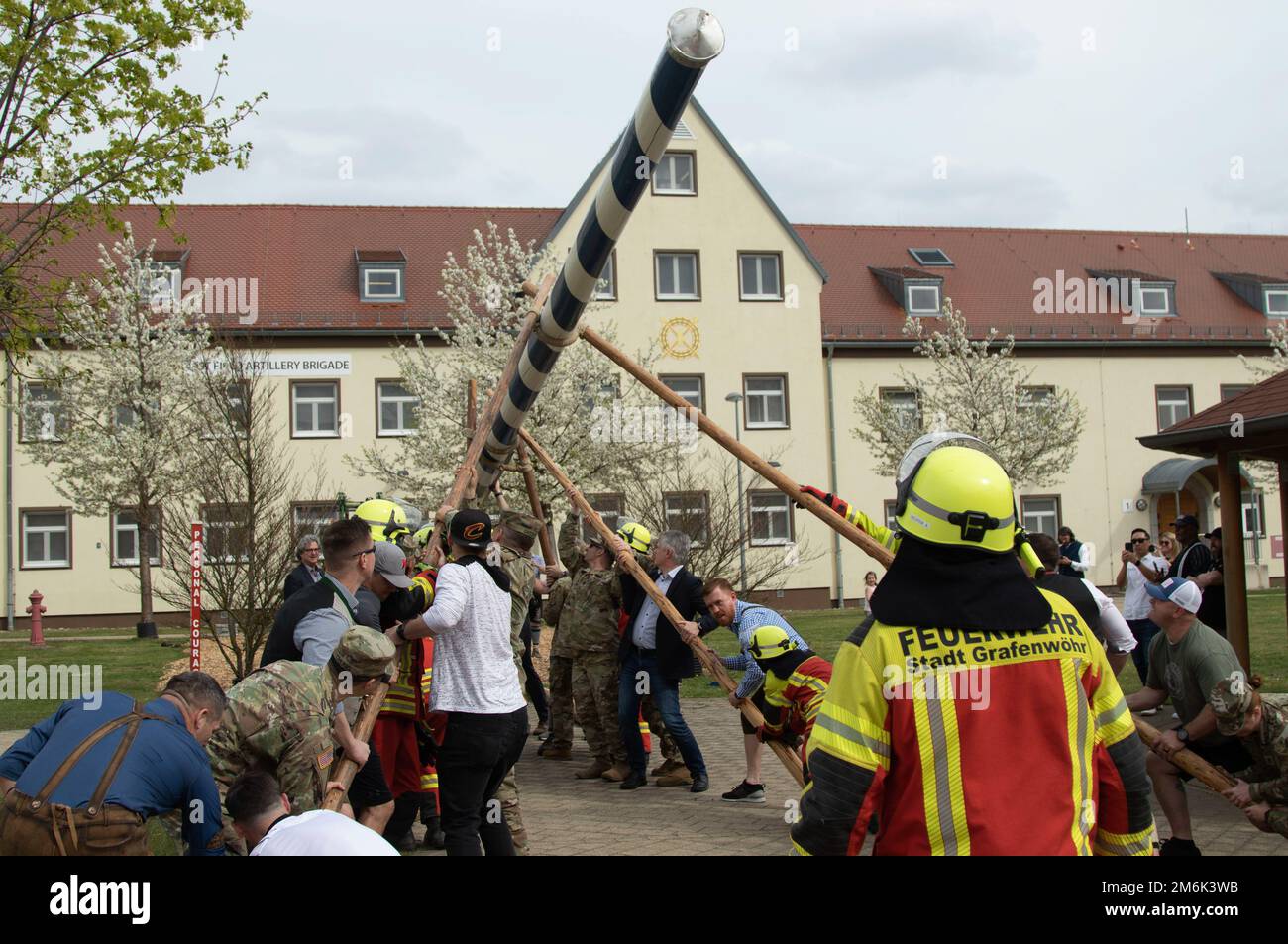 Chief of the Grafenwoehr Fire Department Alexander Richter directs a group of people including 41st Field Artillery Brigade leadership and local government  representatives in raising a Maypole at Grafenwoehr Training Area, Germany April 29, 2022. Maypole, or “Maibaum” in German, dates back to the 16th century and is celebrated in many places across Europe. The tradition centers on the raising of a large, decorated tree trunk in the town center followed by traditional Bavarian festivities. Stock Photo