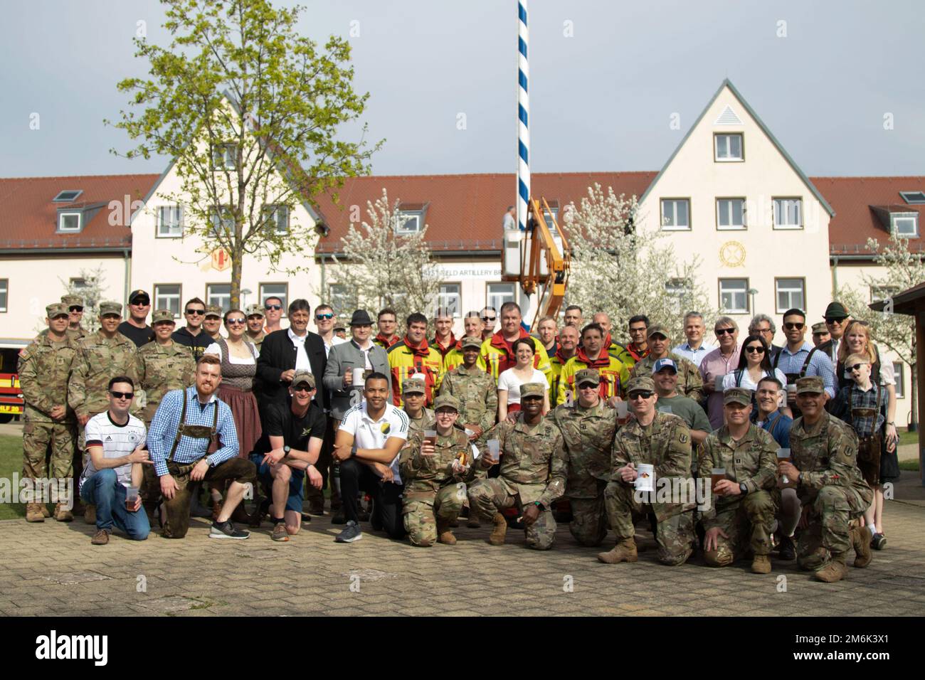 Local Bavarian representatives alongside the 41st Field Artillery Brigade leadership and their friends and family pose in front of the Maypole they raised during the Inaugural Maypole celebration at the 41st FAB’s Headquarters building in Grafenwoehr Training area, Germany April 29, 2022. Maypole, or “Maibaum” in German, dates back to the 16th century and is celebrated in many places across Europe. The tradition centers on the raising of a large, decorated tree trunk in the town center followed by traditional Bavarian festivities. Stock Photo