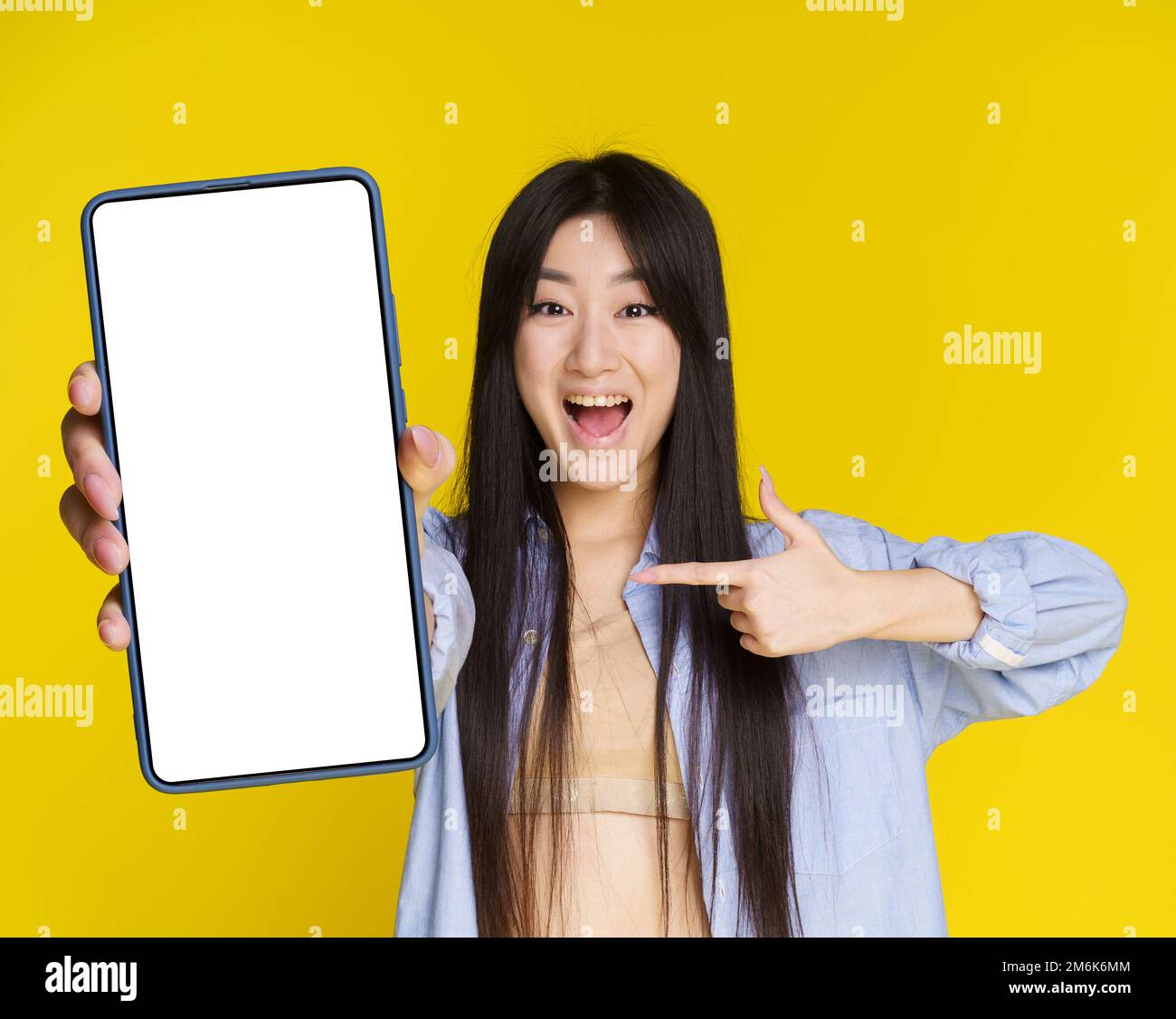 Asian girl excited win, lottery, casino, game, sale offer holding smartphone pointing on empty screen isolated on yellow backgro Stock Photo