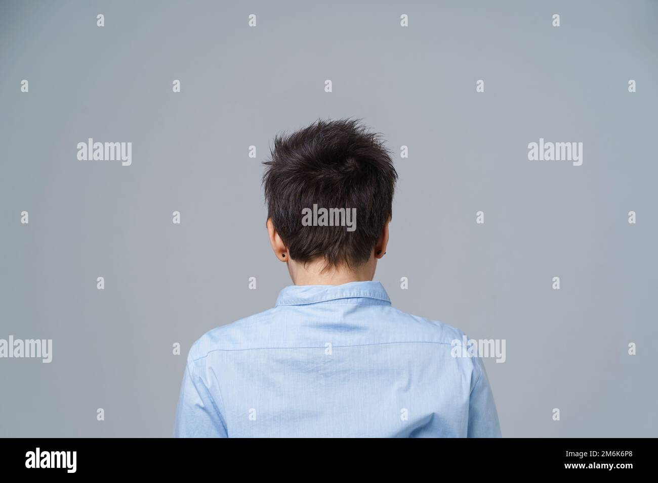 Grey short hair mature woman posing standing back to camera in blue shirt isolated on white background. Aged beauty Stock Photo