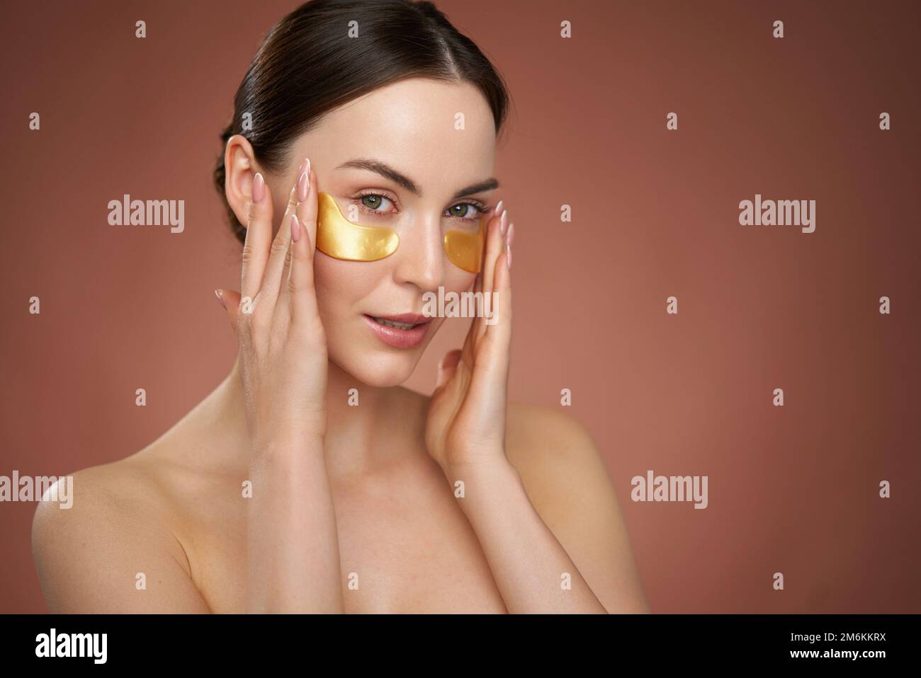 Woman applying eye patches on brown background Stock Photo