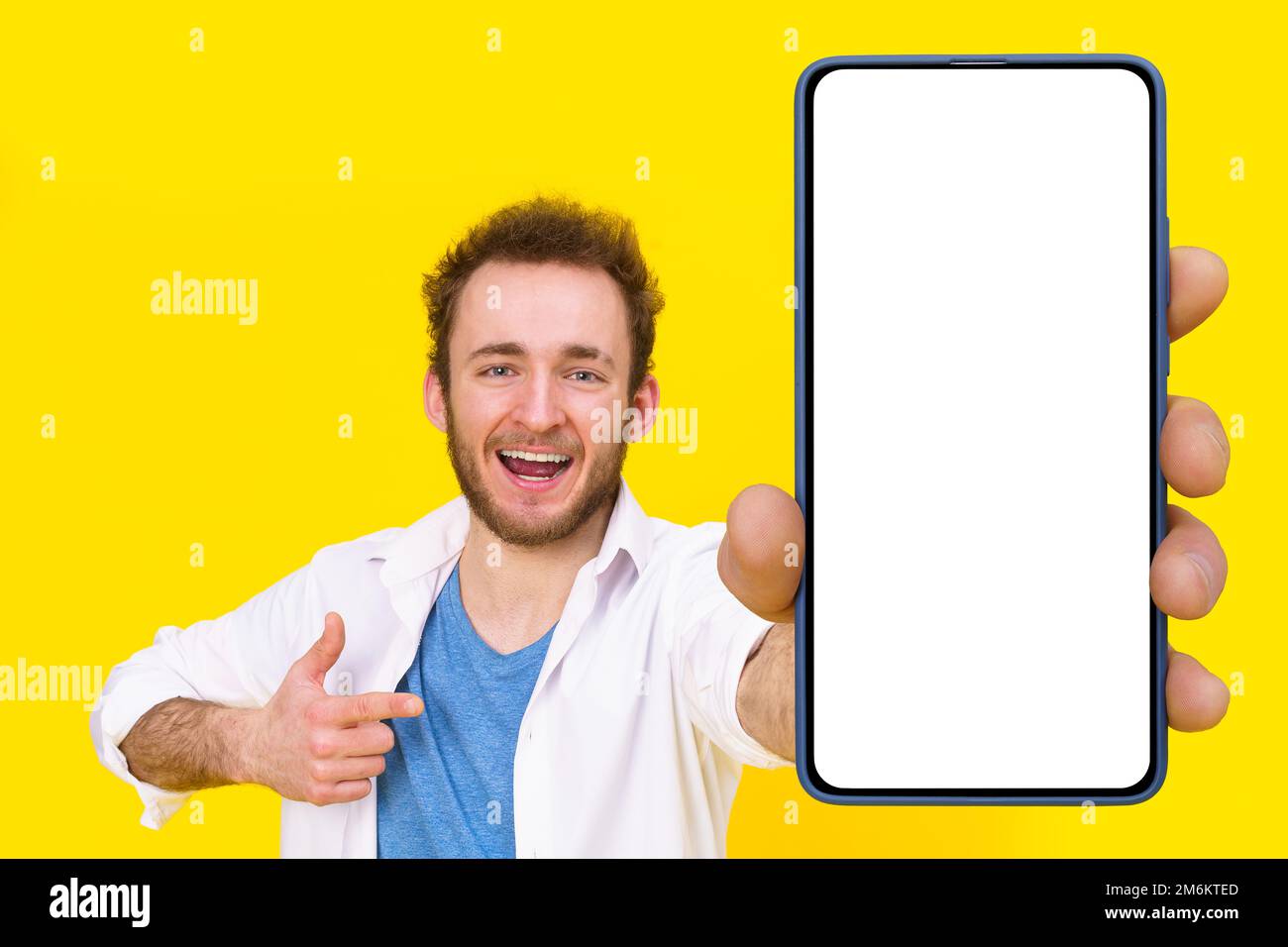 Check this app young man pointing at smartphone showing a white empty screen game, bet, lottery win isolated over yellow backgro Stock Photo