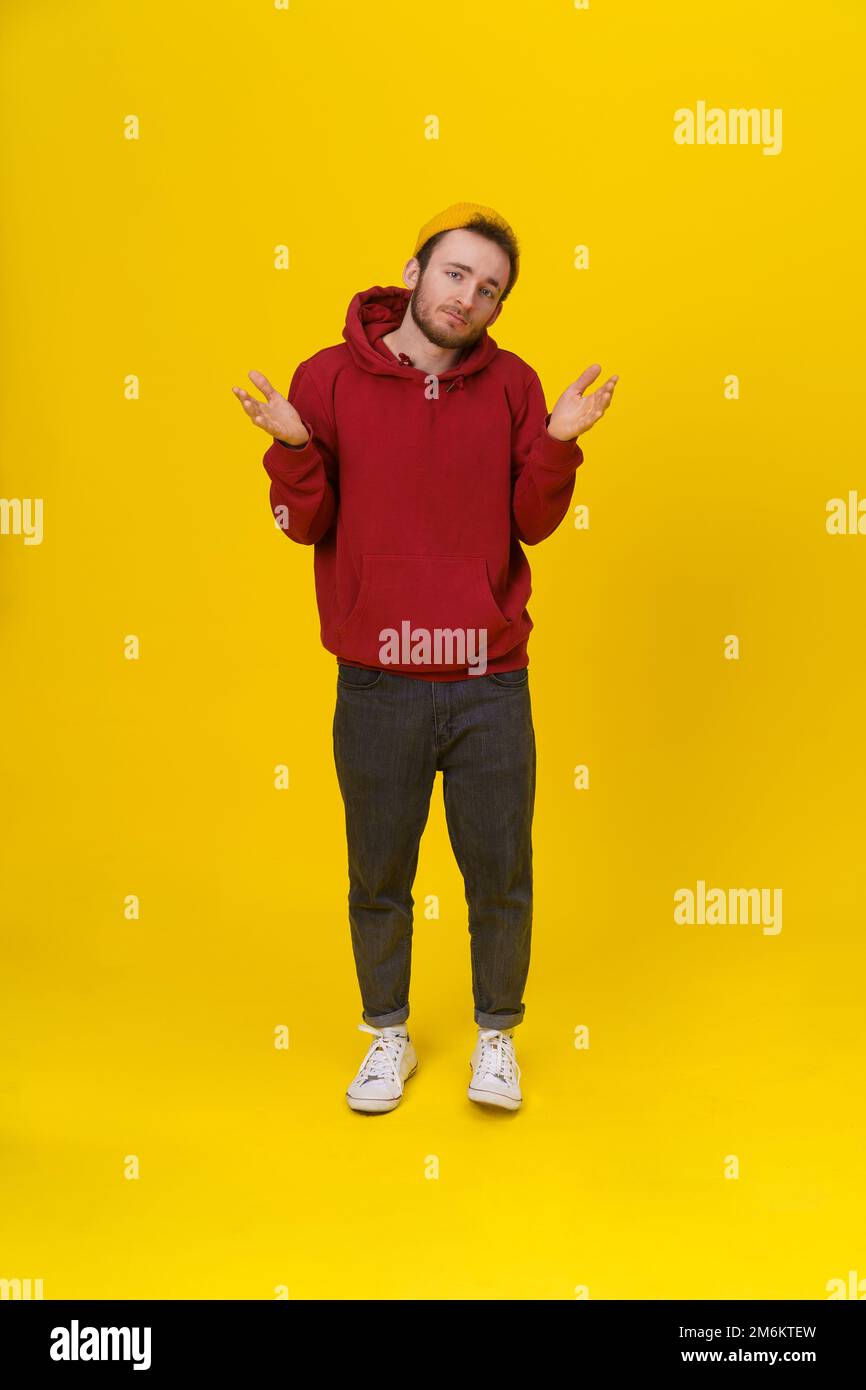 Gesturing with both hands I DONT KNOW handsome young man in casual wear, with hands lifted up looking at camera on yellow backgr Stock Photo