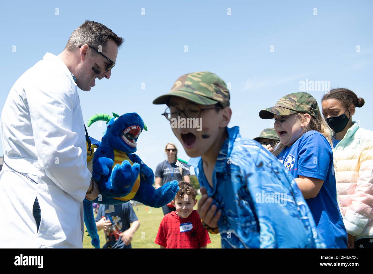 Operation Kids Understanding Deployment Operations participants react as U.S. Army Capt. Ryan Shealy, Camp Zama Dental Health Activity Japan dental clinic officer in charge, left, sprays water out of a dental health stuffed dragon as part of Operation K.U.D.O.S. at Yokota Air Base, Japan, April 30, 2022. Operations K.U.D.O.S. consisted of toy weapon training, a C-130J Super Hercules tour and a mock medical checkup to simulate a deployed environment. Stock Photo