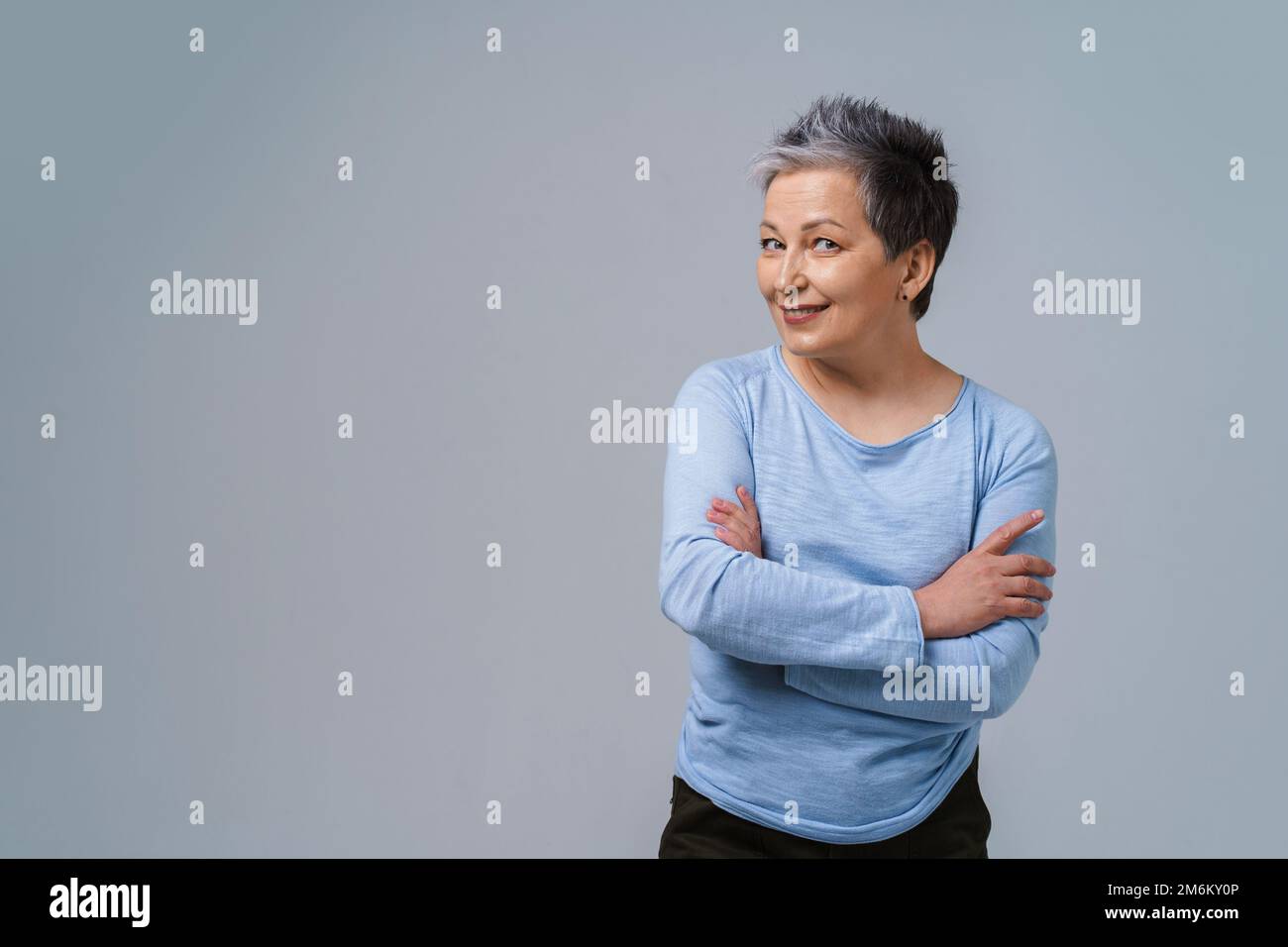 Challenging look positive emotions mature grey hair woman posing with hands folded looking at camera wearing blue blouse, isolat Stock Photo