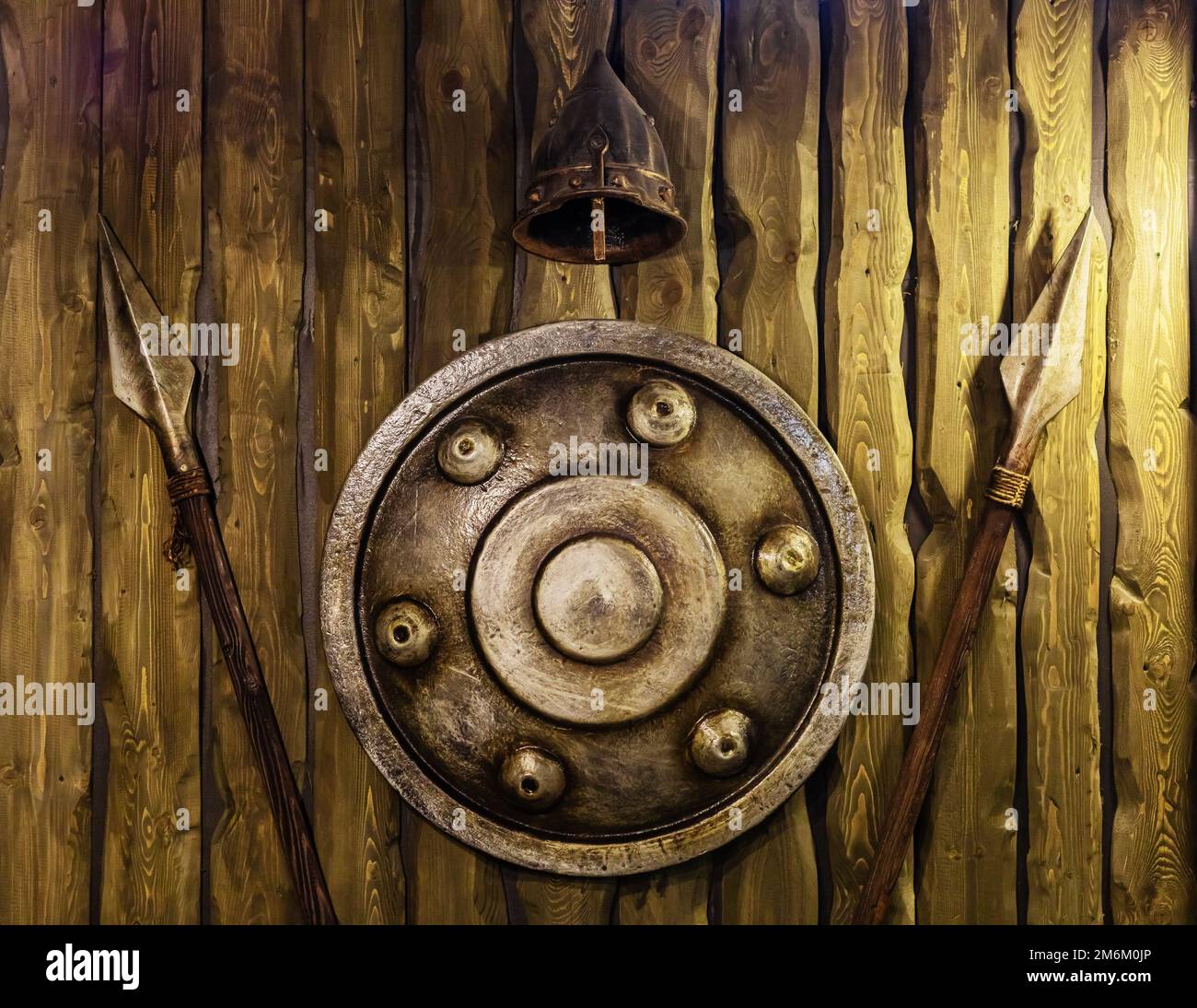 A bronze shield helmet and spears hang on a wooden wall. Knight armour