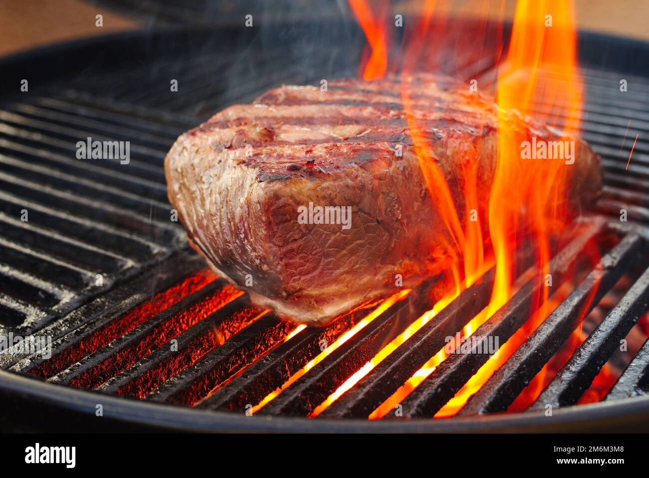 Barbecue dry aged wagyu roast beef steak grilled as closeup on a charcoal grill with fire and