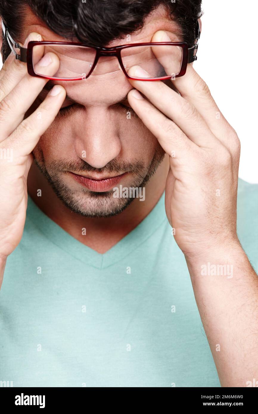 My head feels like its about to explode. A young man rubbing his forehead from stress while isolated on a white background. Stock Photo