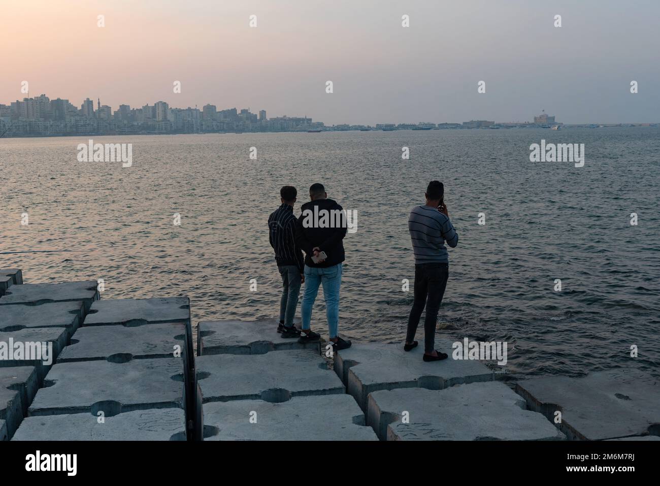 Alexandria, Egypt. December 1st 2022 People on concrete blocks positioned as a defence against rising sea levels along the Corniche of Alexandria, the Stock Photo