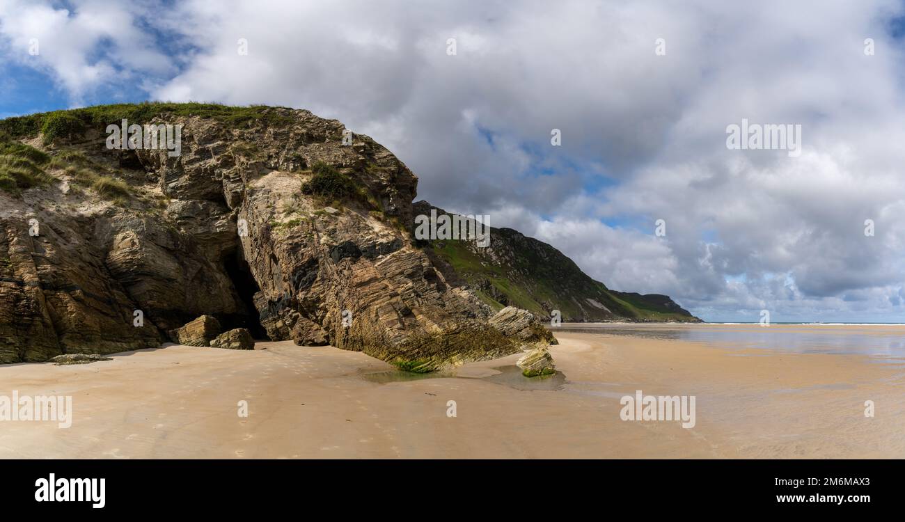 A panorama landscape view of Maghera Beach with the entrance to one of the caves in the rocks Stock Photo