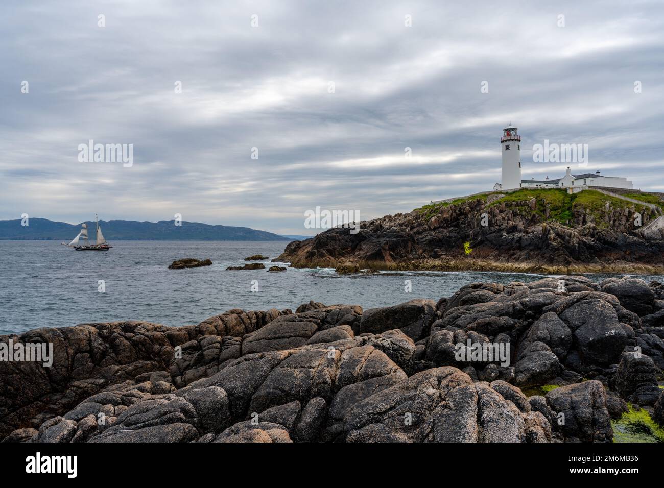 A view of the Fanad Head Lighthouse on the northern coast of Ireland with an old two-masted sailboat Stock Photo