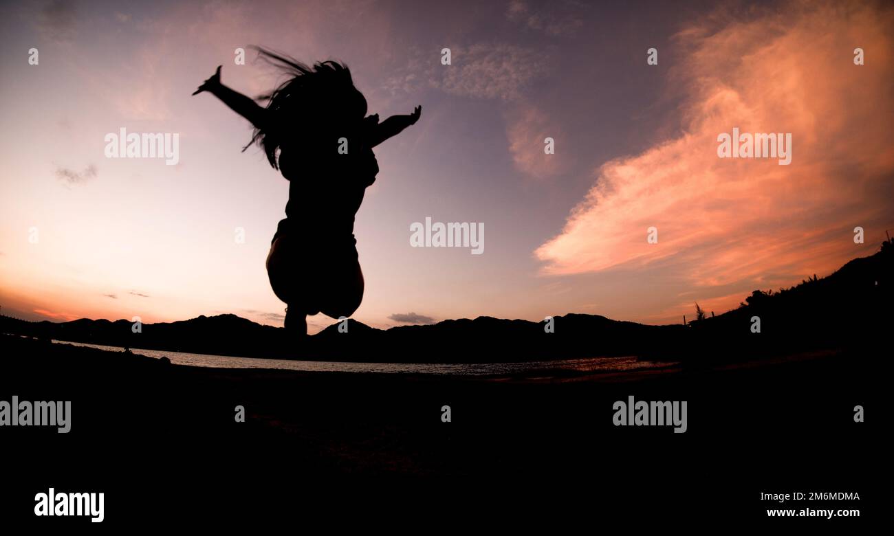 Silhouette, happy jumping Shadow girl Jump on the orange sky in the evening Stock Photo