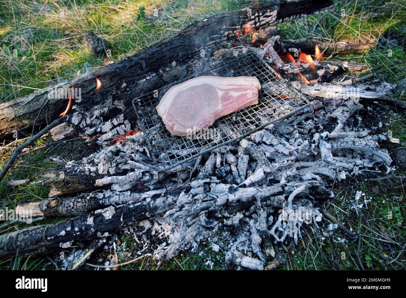 a pork chop is roasting on a small grill on the embers of campfire in Sicily, Etna Park, Italy Stock Photo