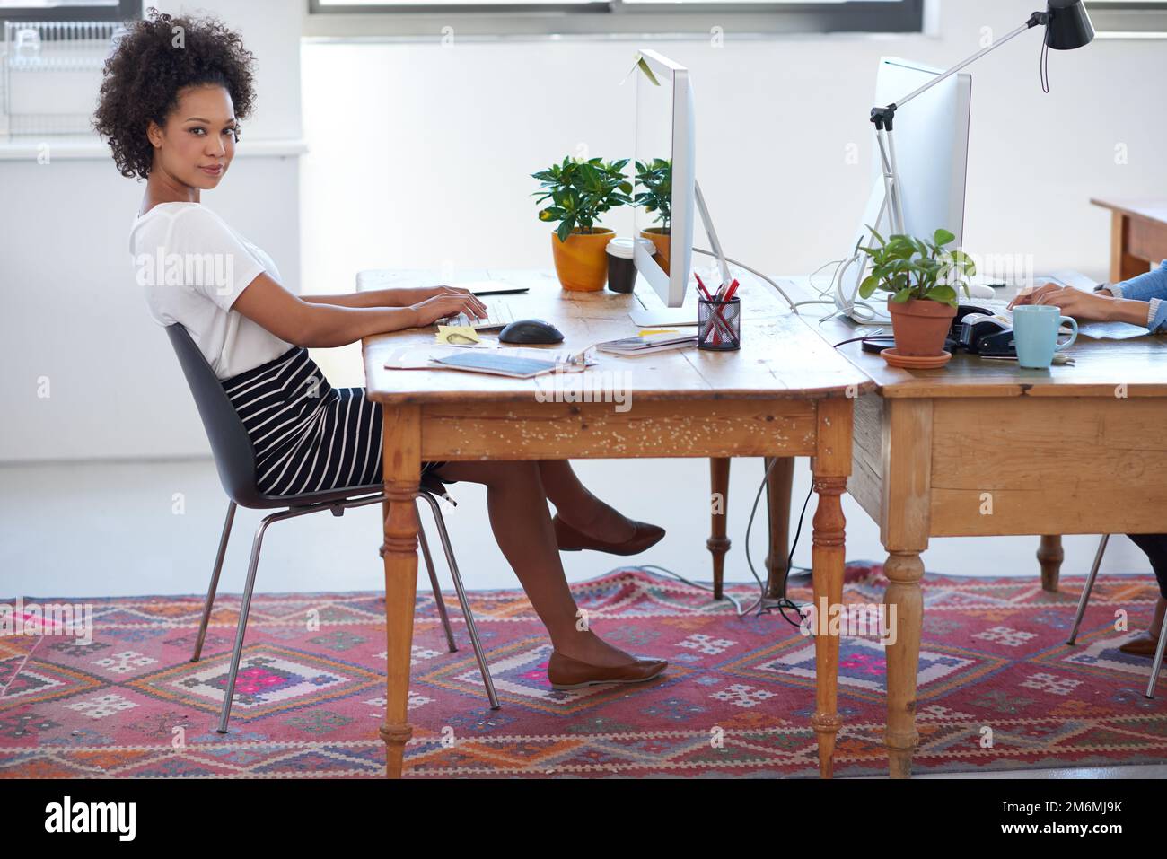 My individual style makes for a creative edge. Beautiful african woman sitting at her desk in an open creative office space. Stock Photo