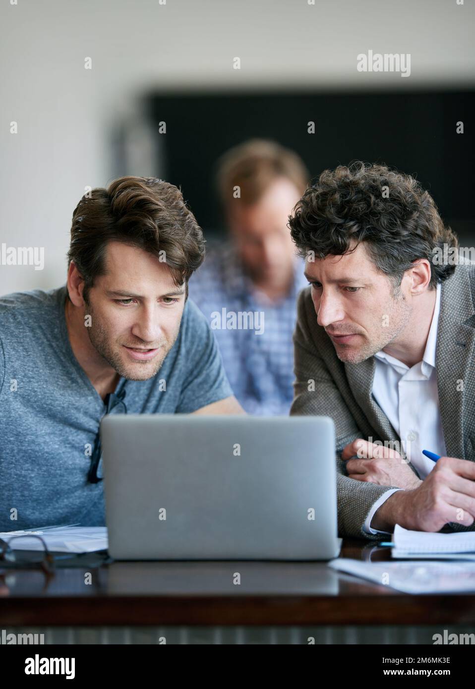 Am I seeing this correctly. two businessmen looking over some work with their colleague in the background. Stock Photo