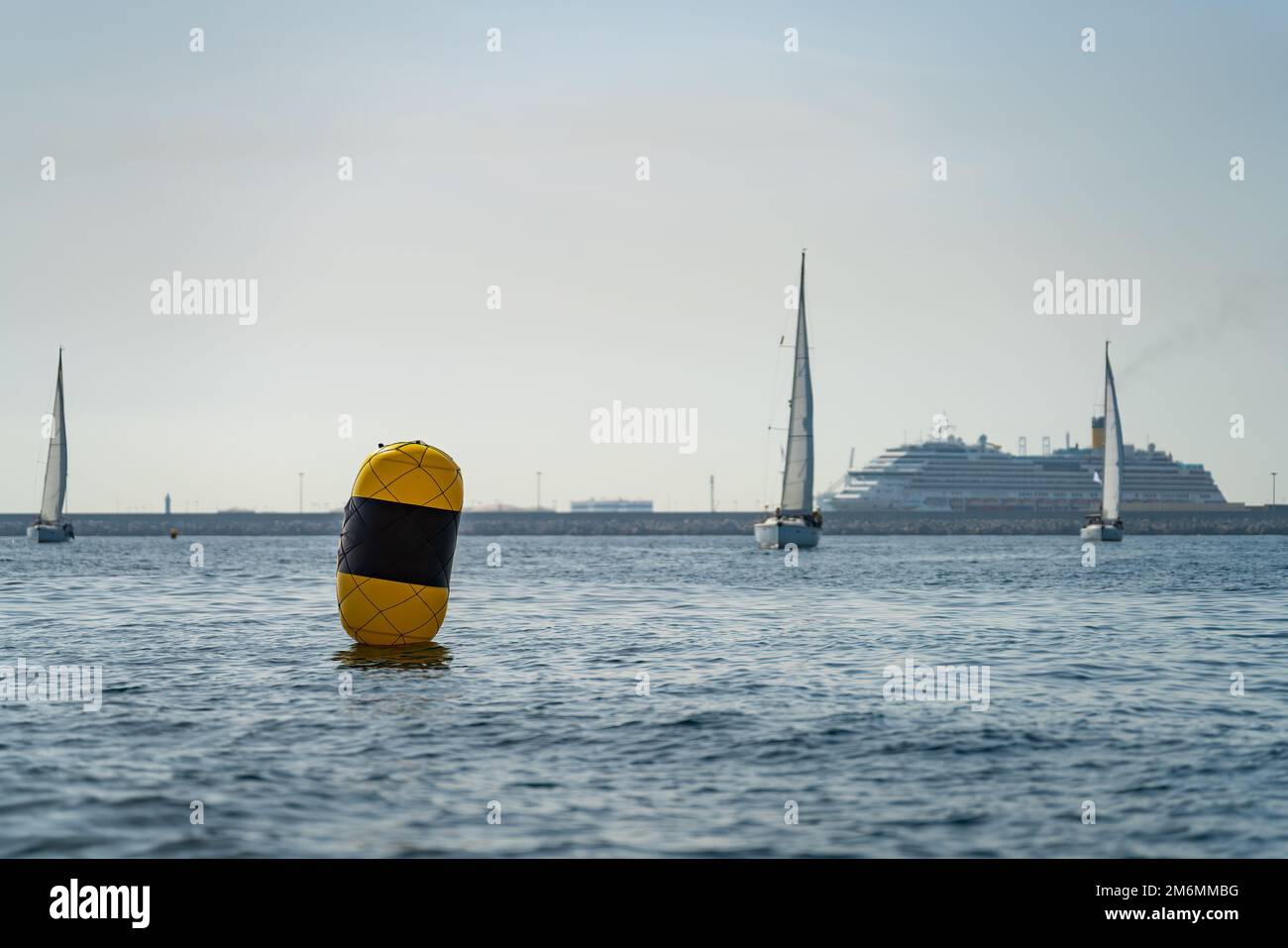 Yellow buoy, blurred sailing ships and passenger ferry in the background Stock Photo
