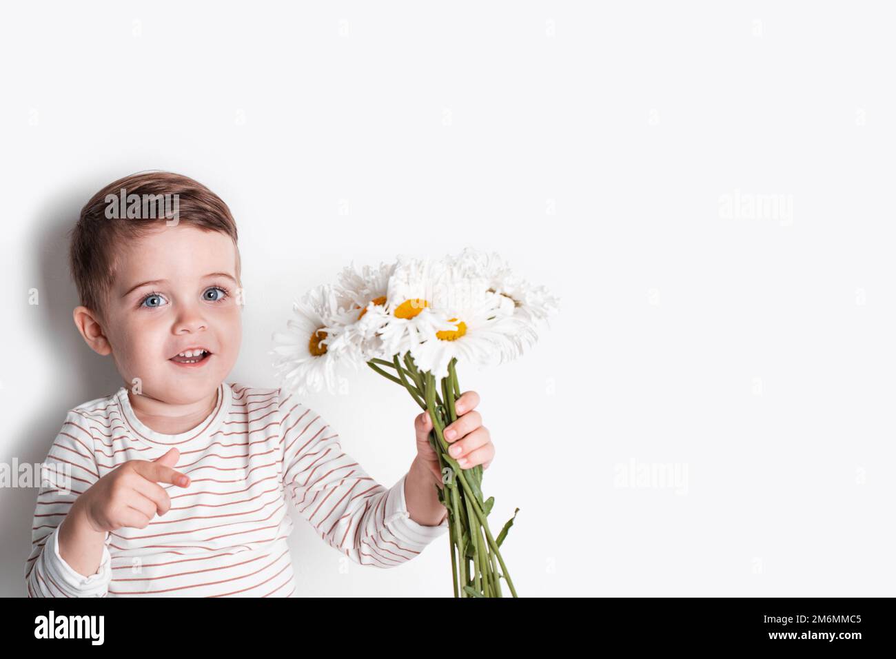 A happy little boy with daisy flowers on white background . A cute smiling child has fun in the summer or spring Stock Photo