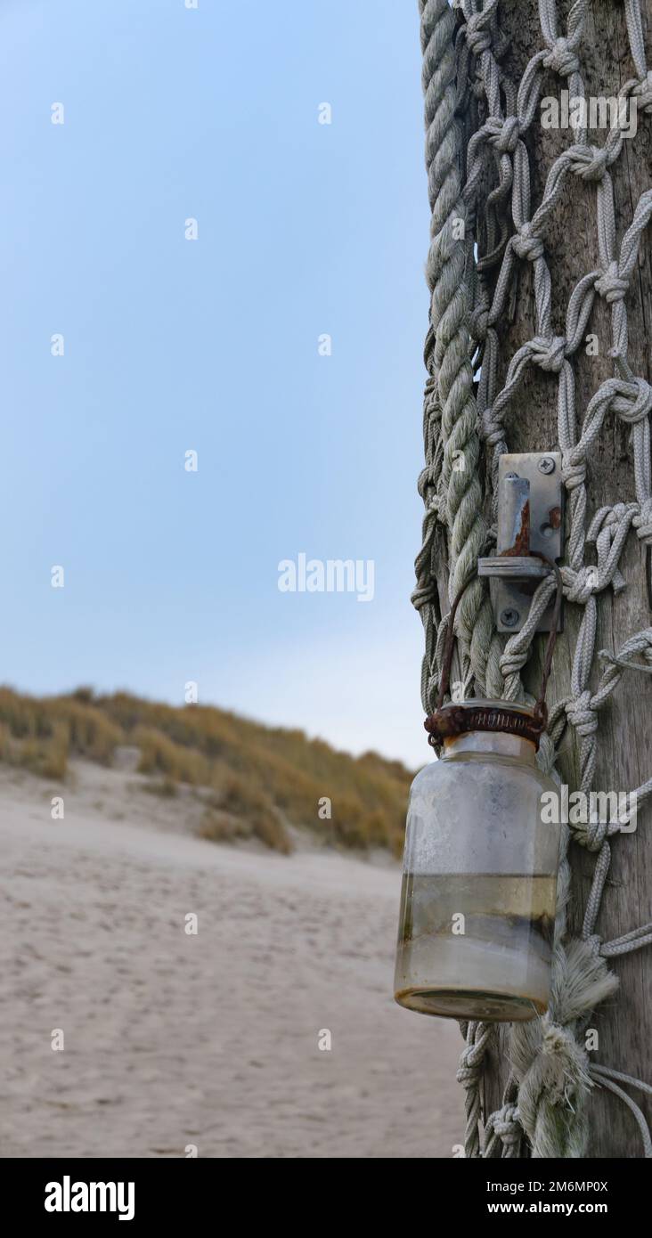 weathered wooden pole with fishing net and glass in front of sand dune