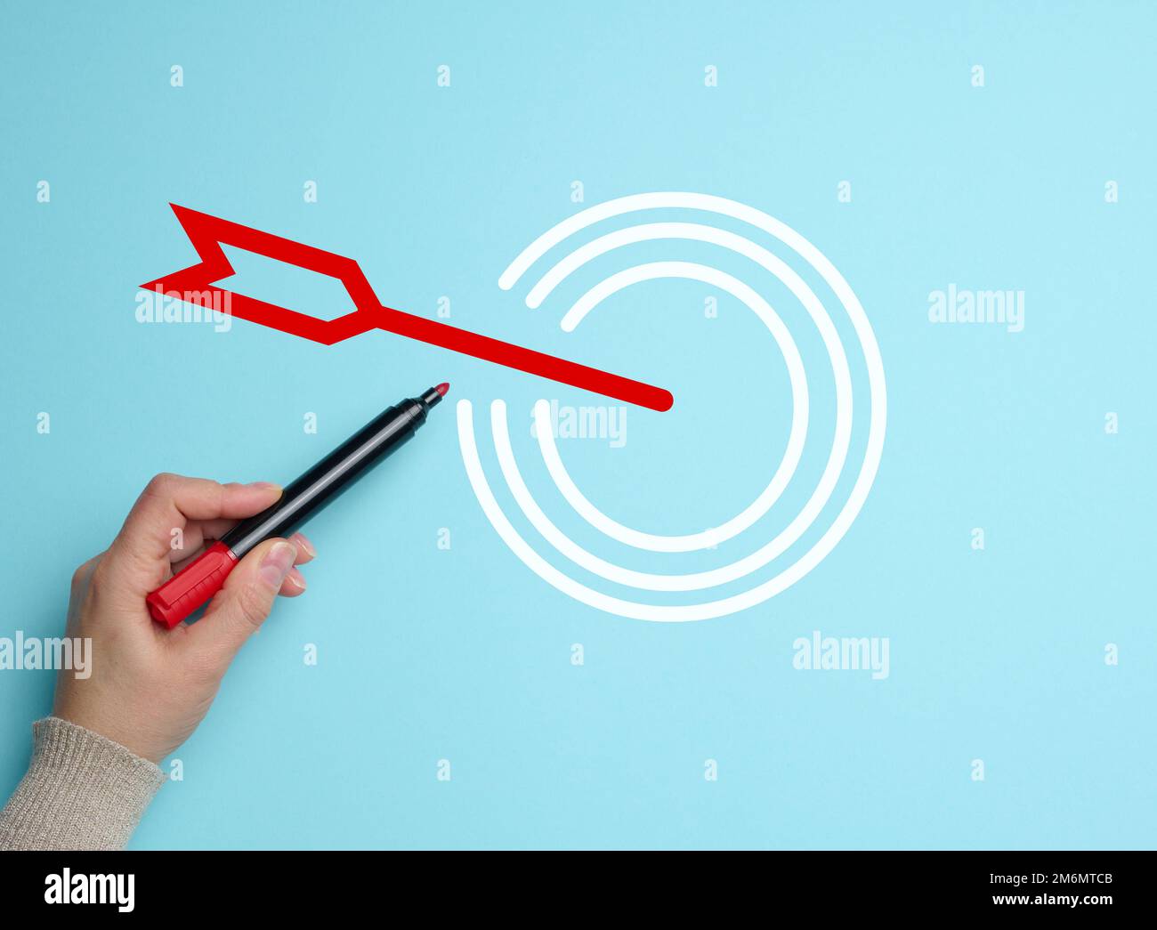 Female hand with marker and target icon on blue background. The concept of achieving set goals, effective management Stock Photo