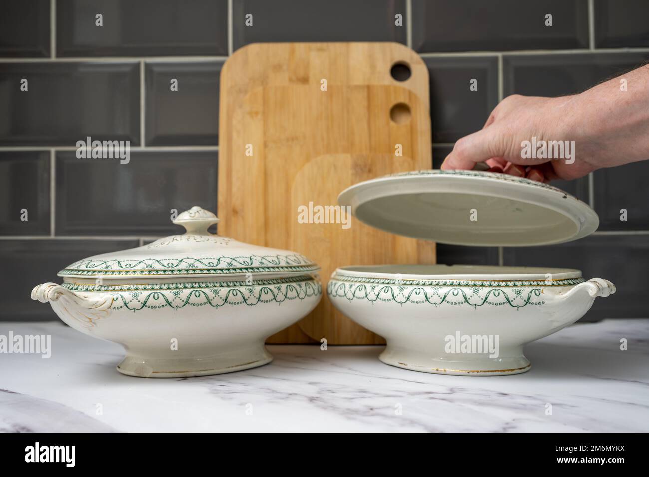 man liting the lid on a tureen to  fill with seasonable vegebales in the kitchen on a marble worktop Stock Photo