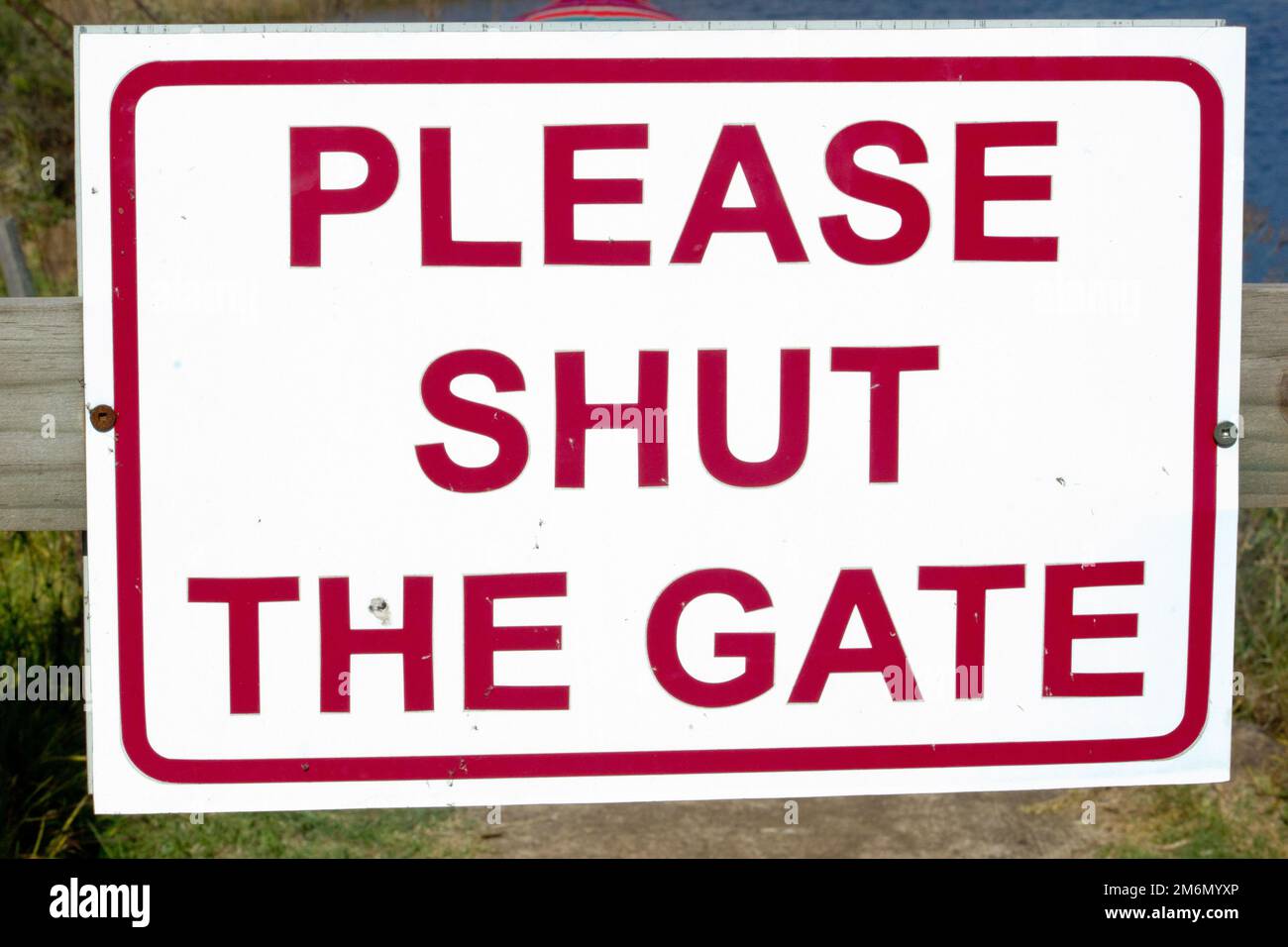 Information sign with words "Please shut the gate" printed in red ink on white metal plate Stock