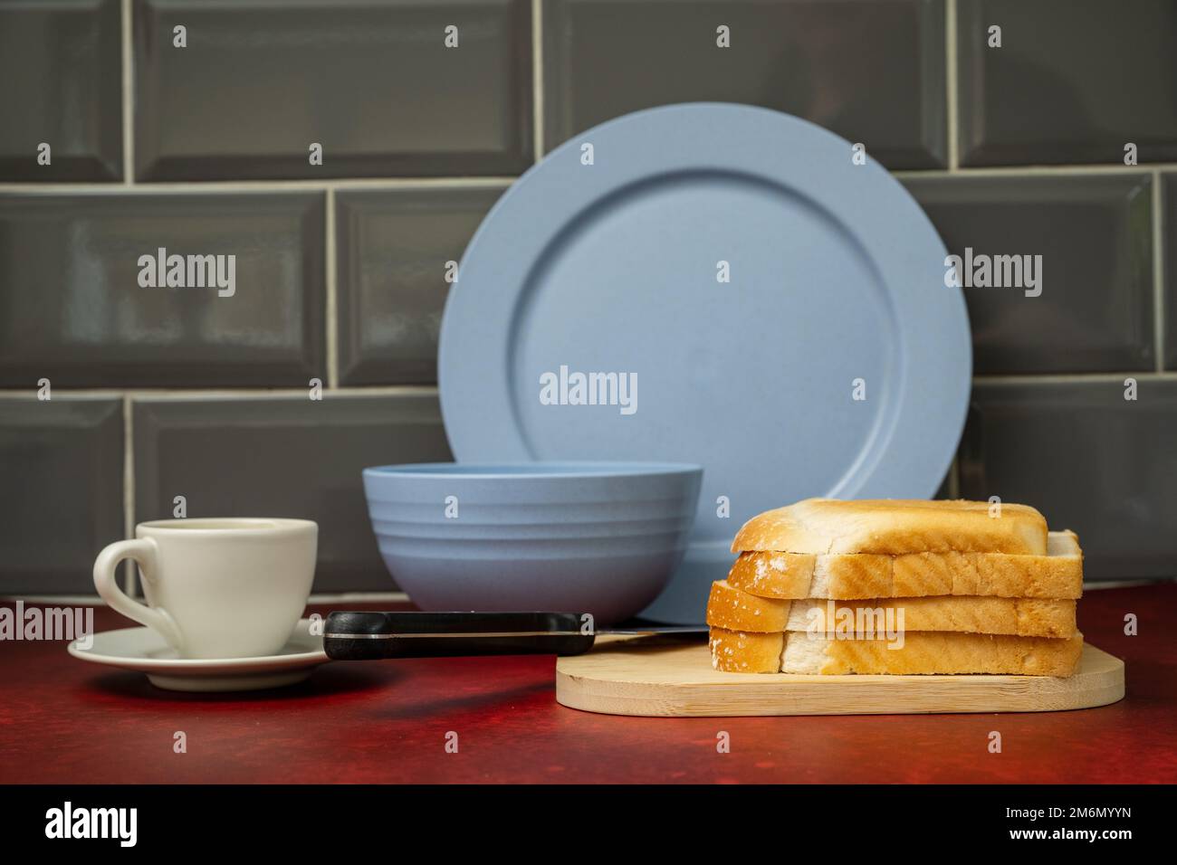 blue  china  dinner plate bowl  expresso coffee cup and saucer  black handled stainless steel knife on wooden board with fresh bread on red linoleum w Stock Photo