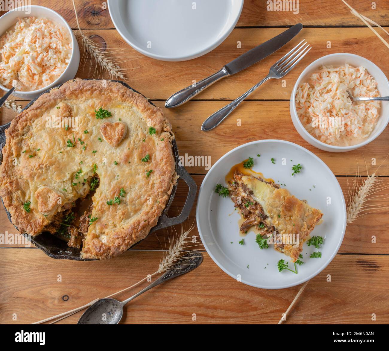 Steak and cheese pie baked in a cast iron pan. Served with fresh coleslaw on wooden table. Flat lay Stock Photo