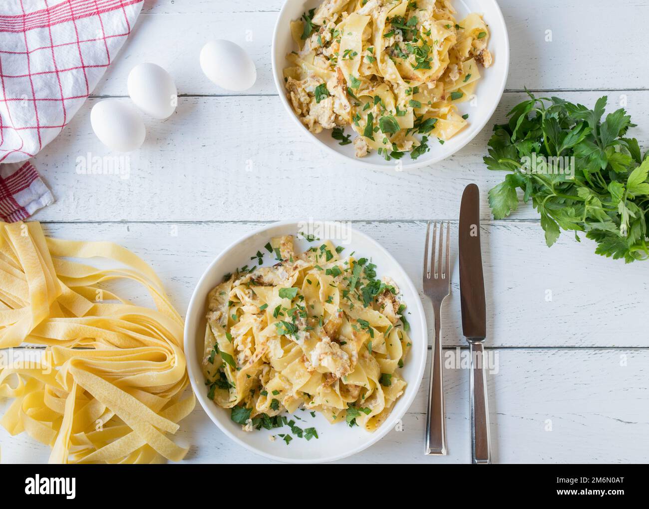 Tagliatelle noodles with scrambled eggs and parsley on plates served on white background with ingredients Stock Photo