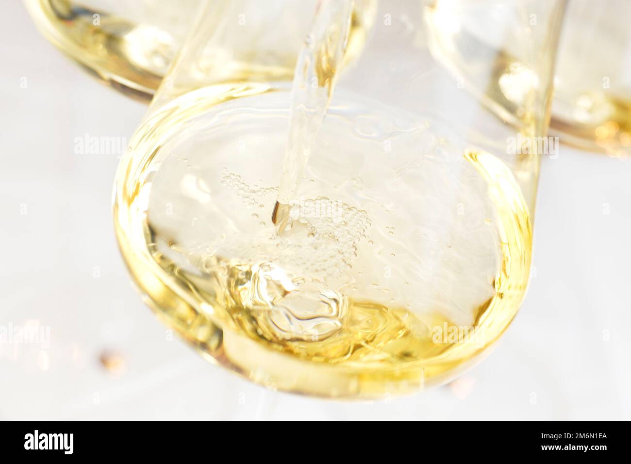 Pouring white wine in a glass with bright background - selective focus on the bubbles Stock Photo